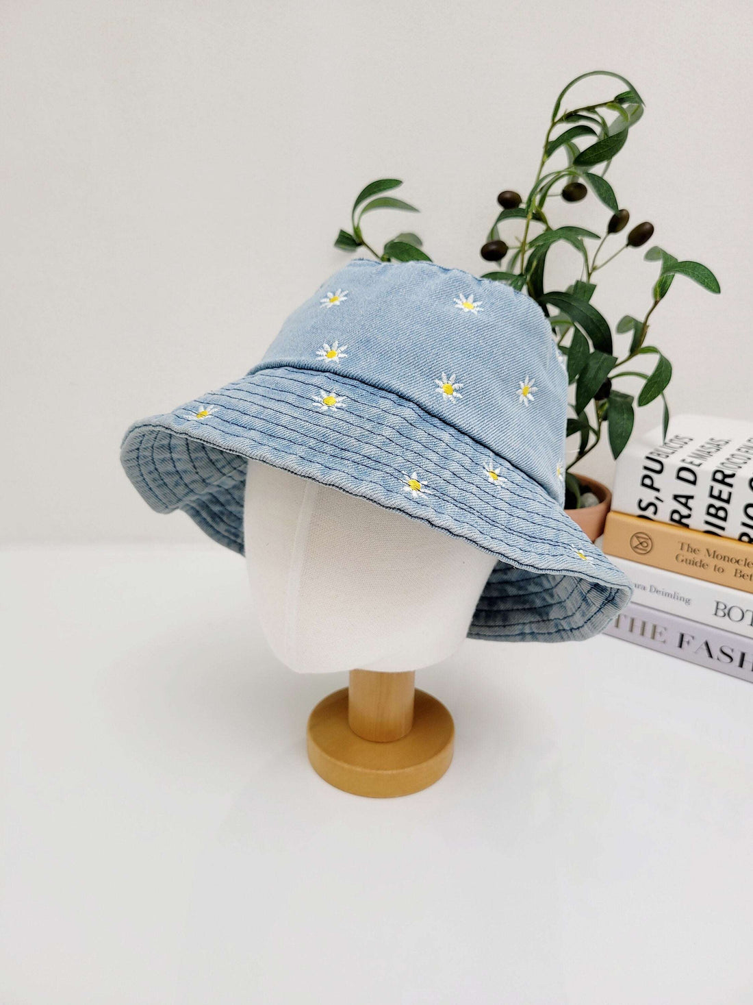 DAISY DENIM bucket hat: Light blue denim hat with embroidered white daisies, displayed on a mannequin head.