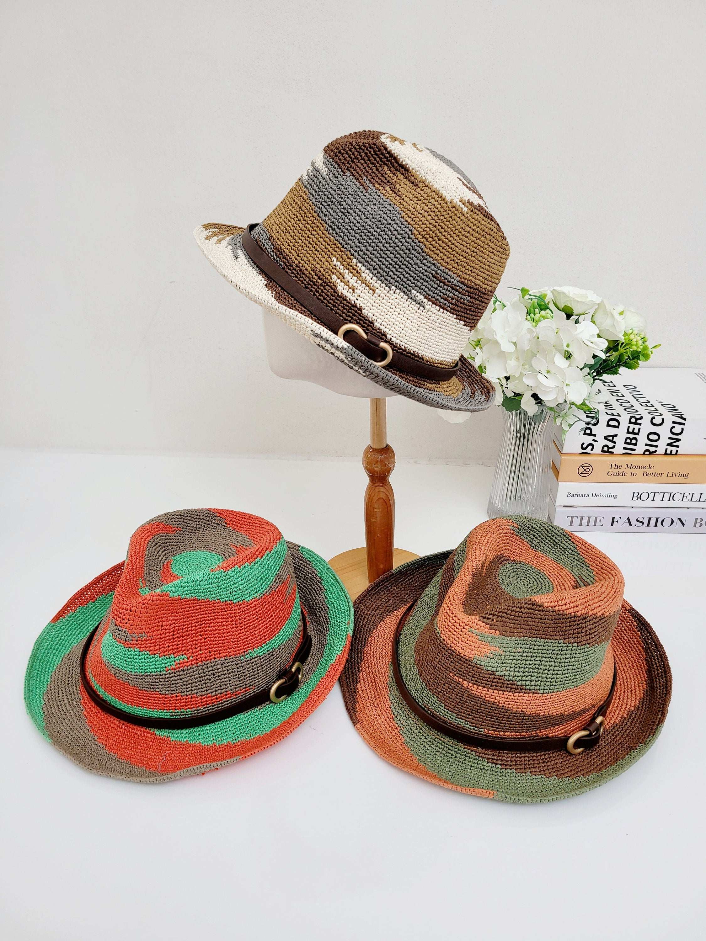 Three SERENGETI woven hats: one neutral-toned on a stand, plus orange/green and brown/green hats on a white surface. Each features a decorative band.