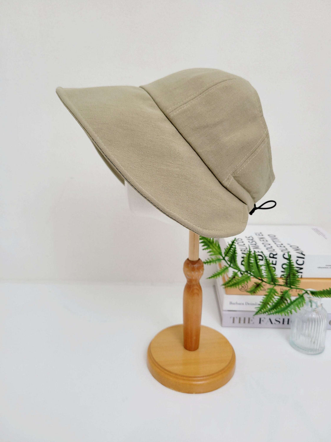 Beige linen sun hat with a wide, downturned brim, displayed on a wooden stand. A stylish and practical summer accessory.