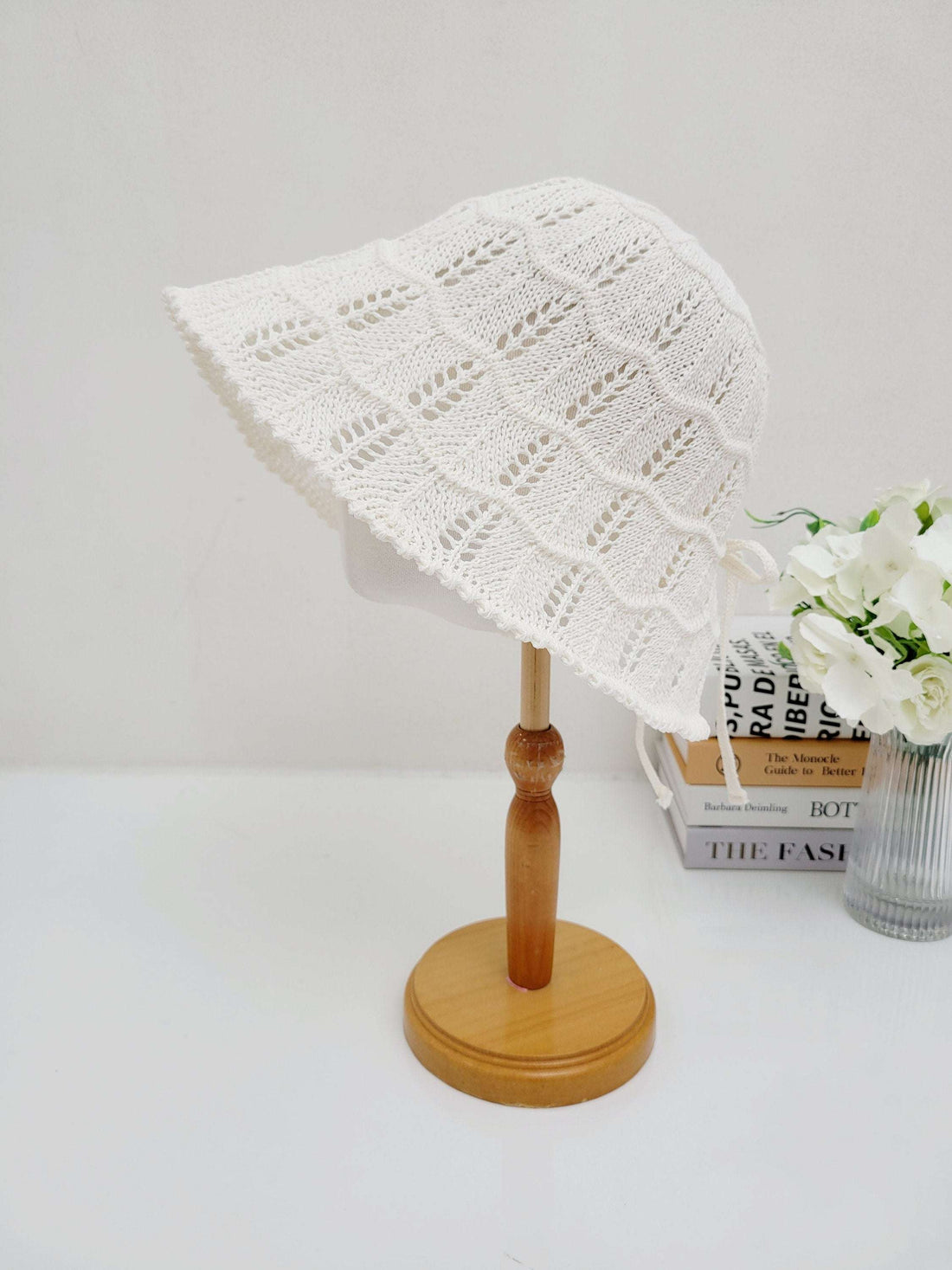 White crocheted bucket hat, ashley's summer favorite, with airy openwork design and wide brim, displayed on a wooden stand.