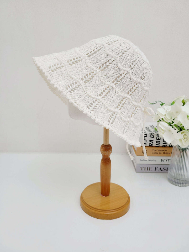 White crocheted bucket hat, ashley's summer favorite, with airy openwork design and wide brim, displayed on a wooden stand.