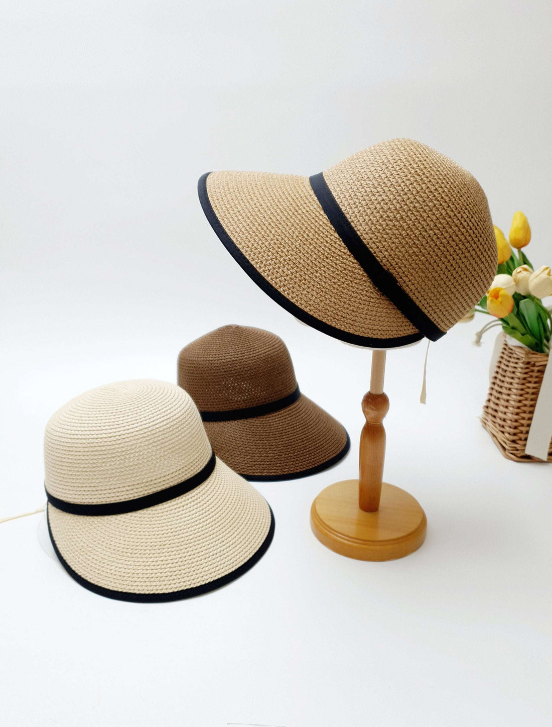 Three straw sun hats: beige with black trim, brown, and a hepburn panama on a stand, all with a wide brim.