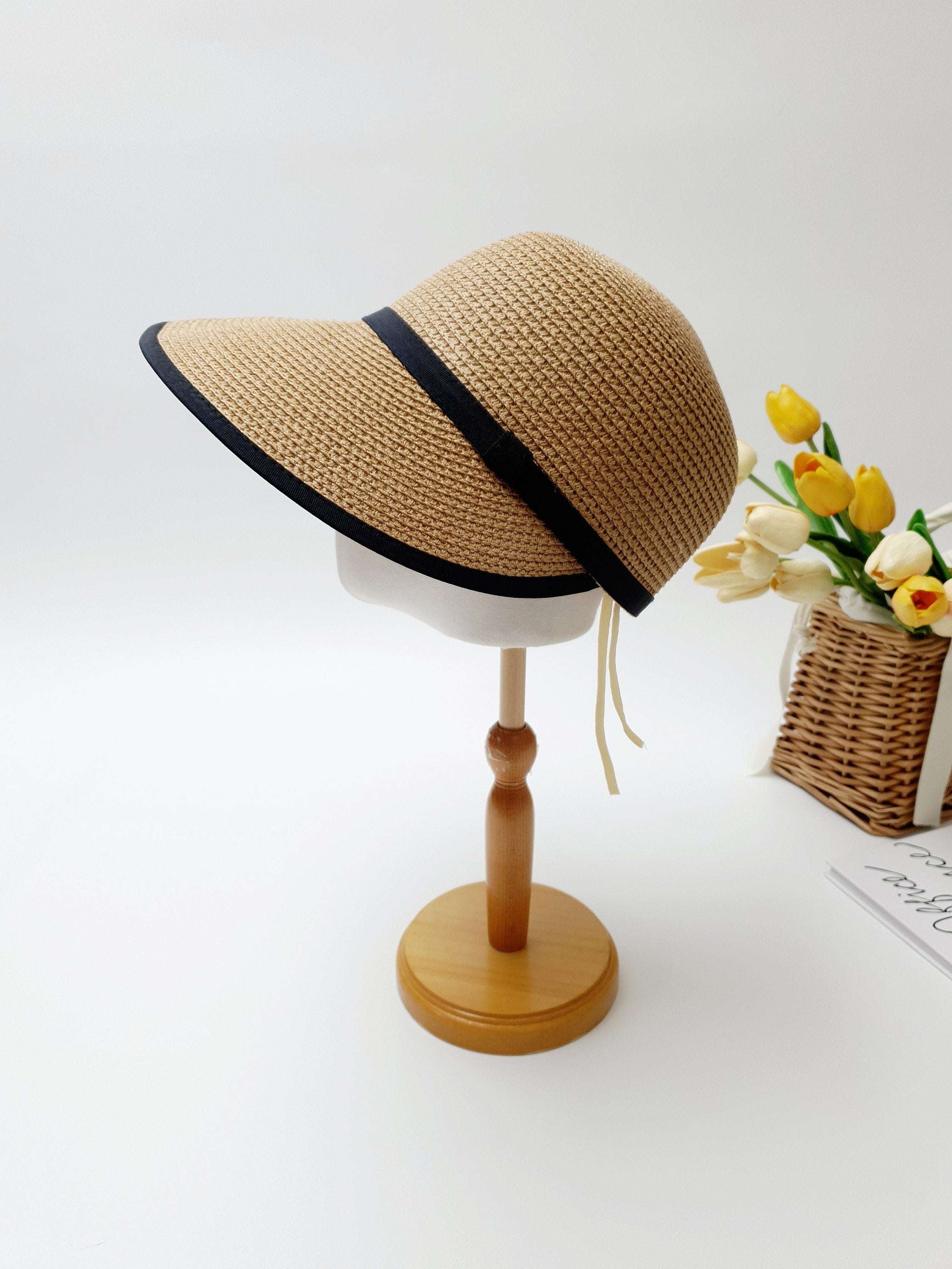 hepburn panama: Beige woven sun visor with stylish black trim, displayed on a wooden stand. Perfect sun protection.