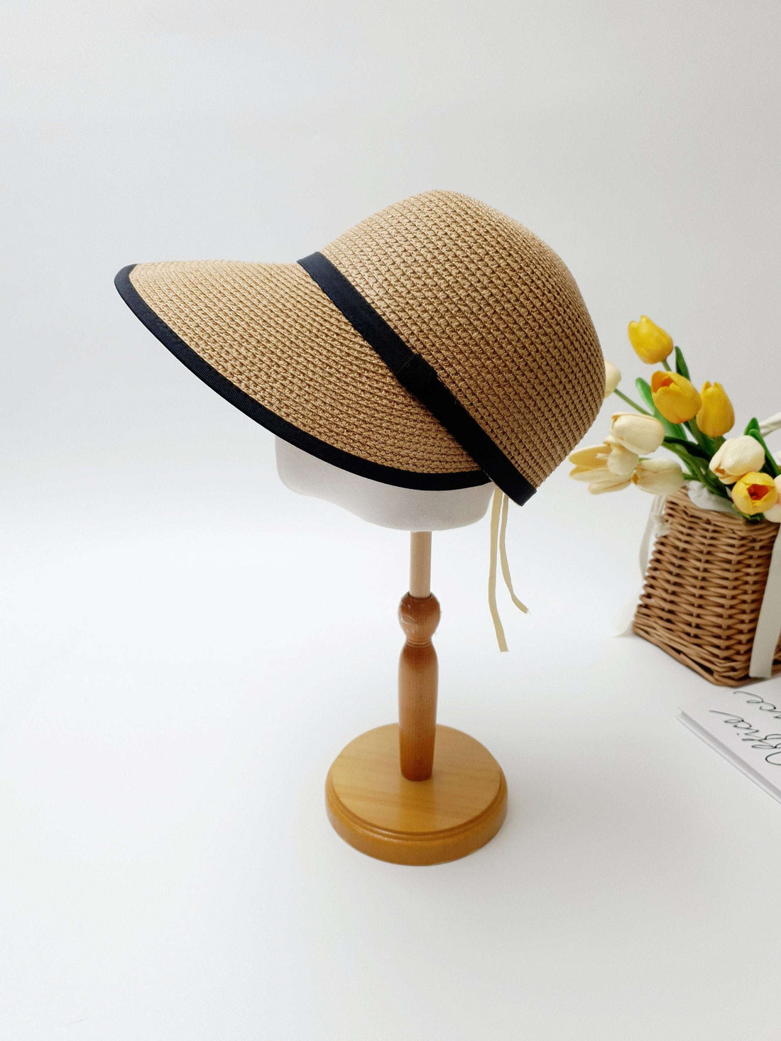 hepburn panama: Beige woven sun visor with stylish black trim, displayed on a wooden stand. Perfect sun protection.