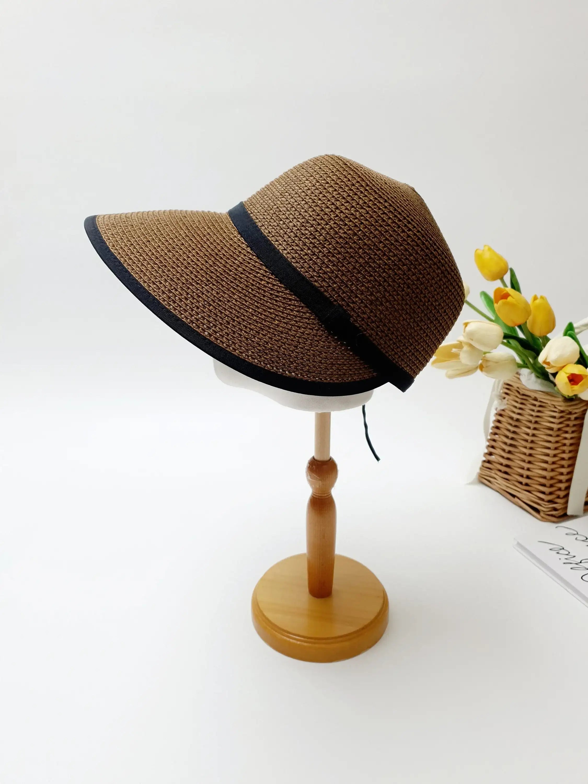 Brown woven hepburn panama sun hat with a stylish black band, displayed on a wooden stand