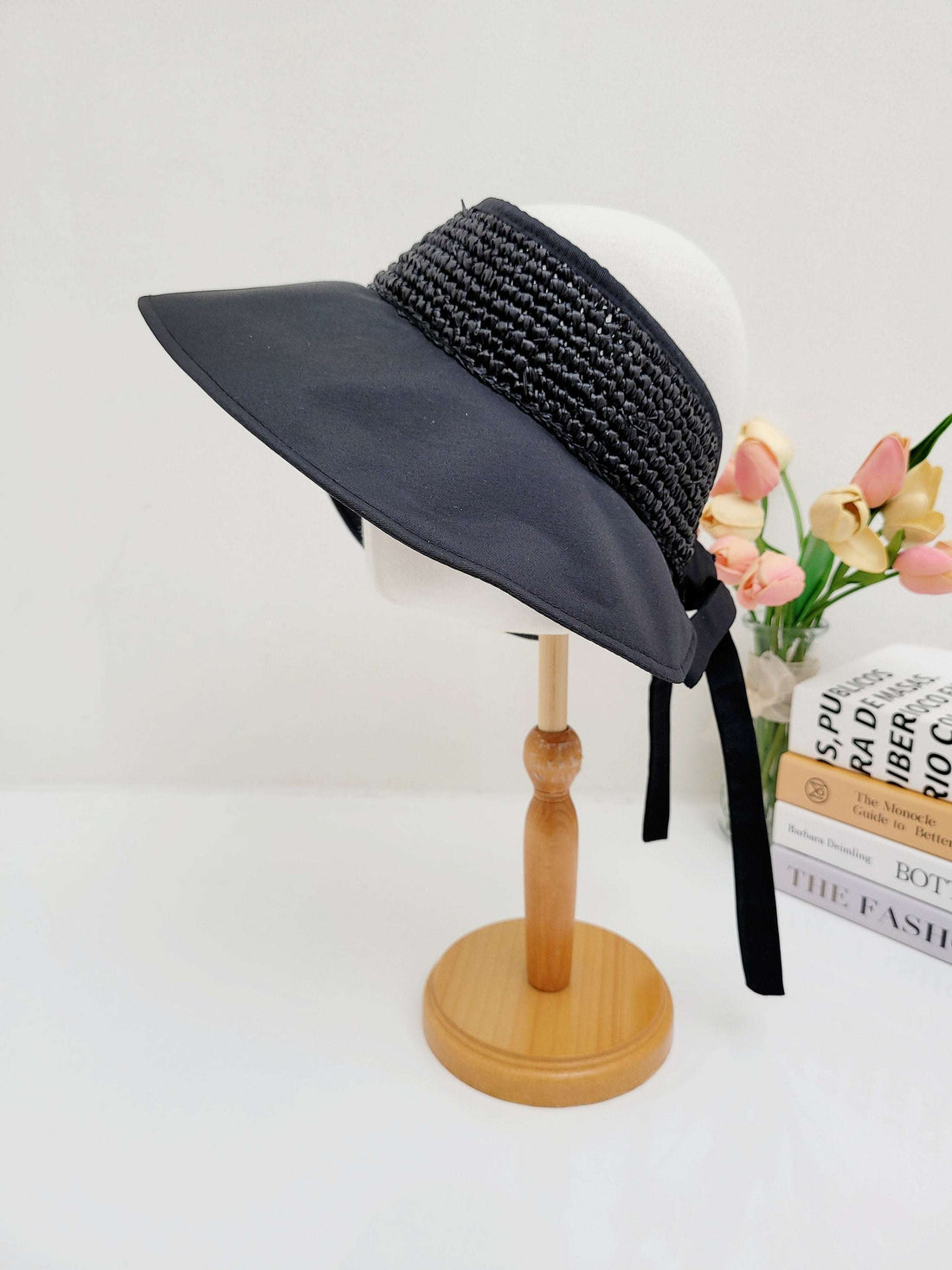 GRAYTON BEACH black sun visor hat with woven band detail and elegant tie closure, displayed on a wooden stand.