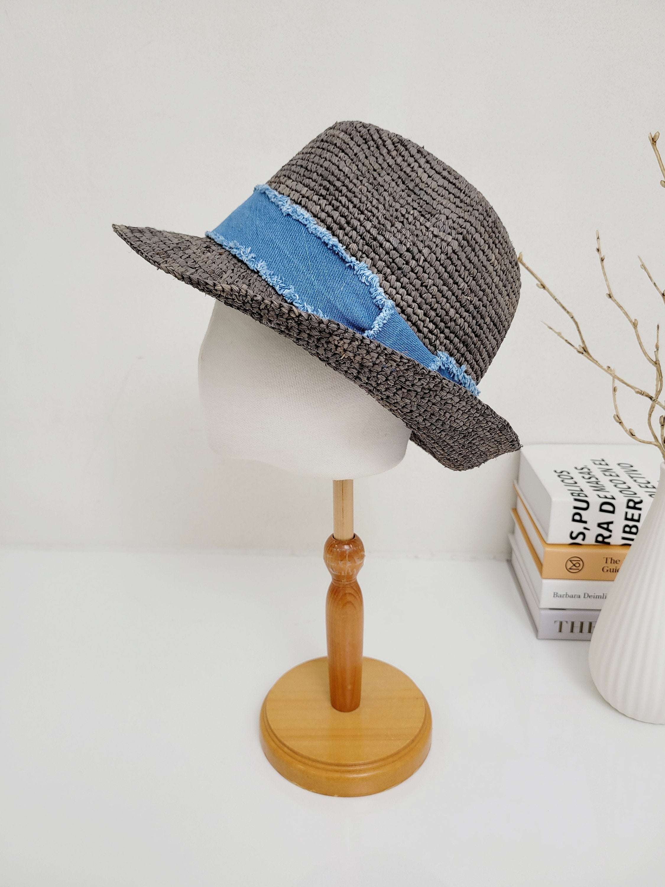 Gray woven lic breeze hat with a frayed light blue denim band, displayed on a wooden stand.