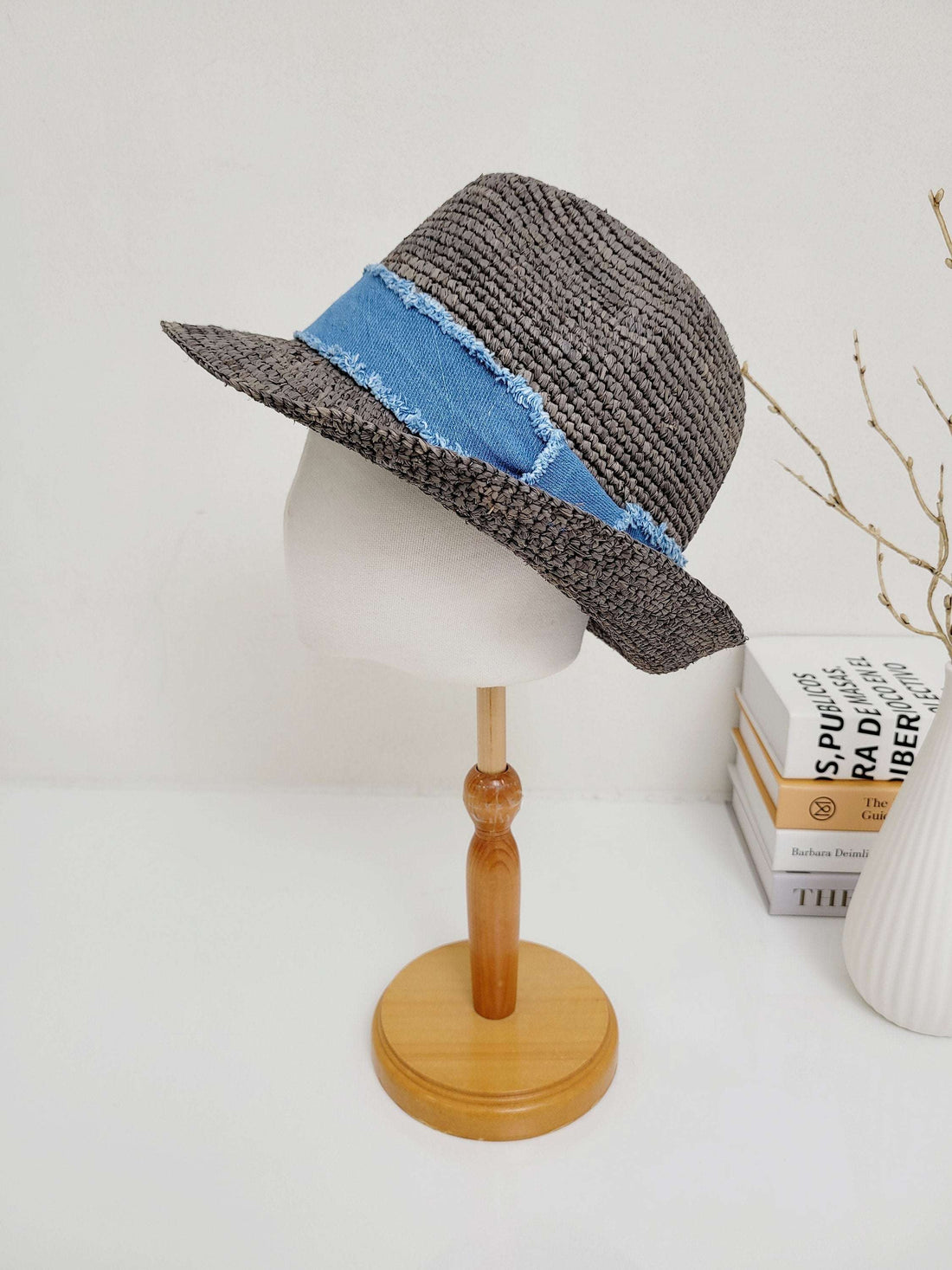 Gray woven lic breeze hat with a frayed light blue denim band, displayed on a wooden stand.