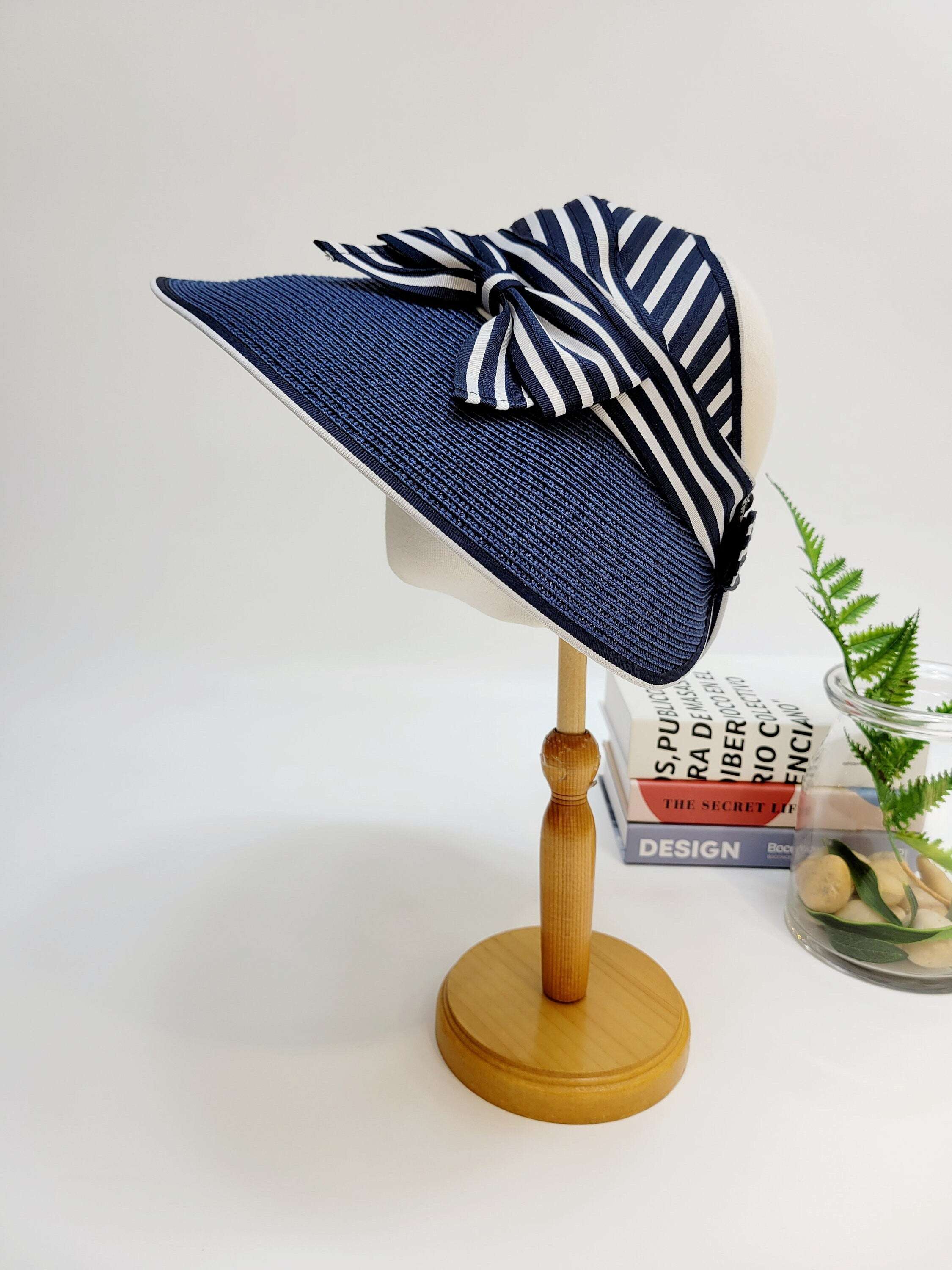 MONROE navy blue sun hat with chic black & white striped bow detail, displayed on a wooden stand.