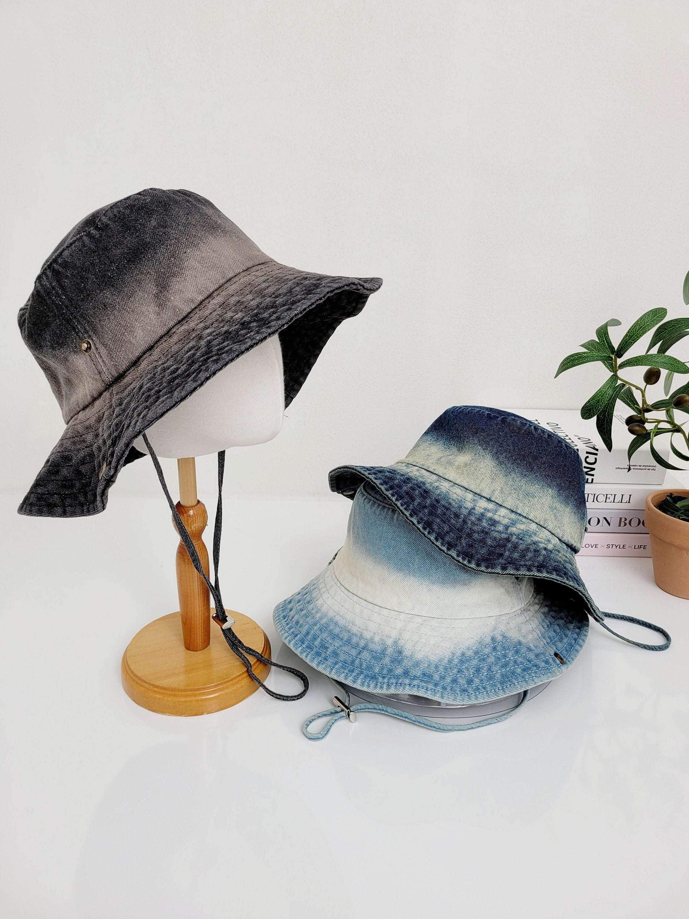 Cotton denim hat display: a dark grey bucket hat on a stand, and two stacked light blue denim hats. Perfect casual sun protection.