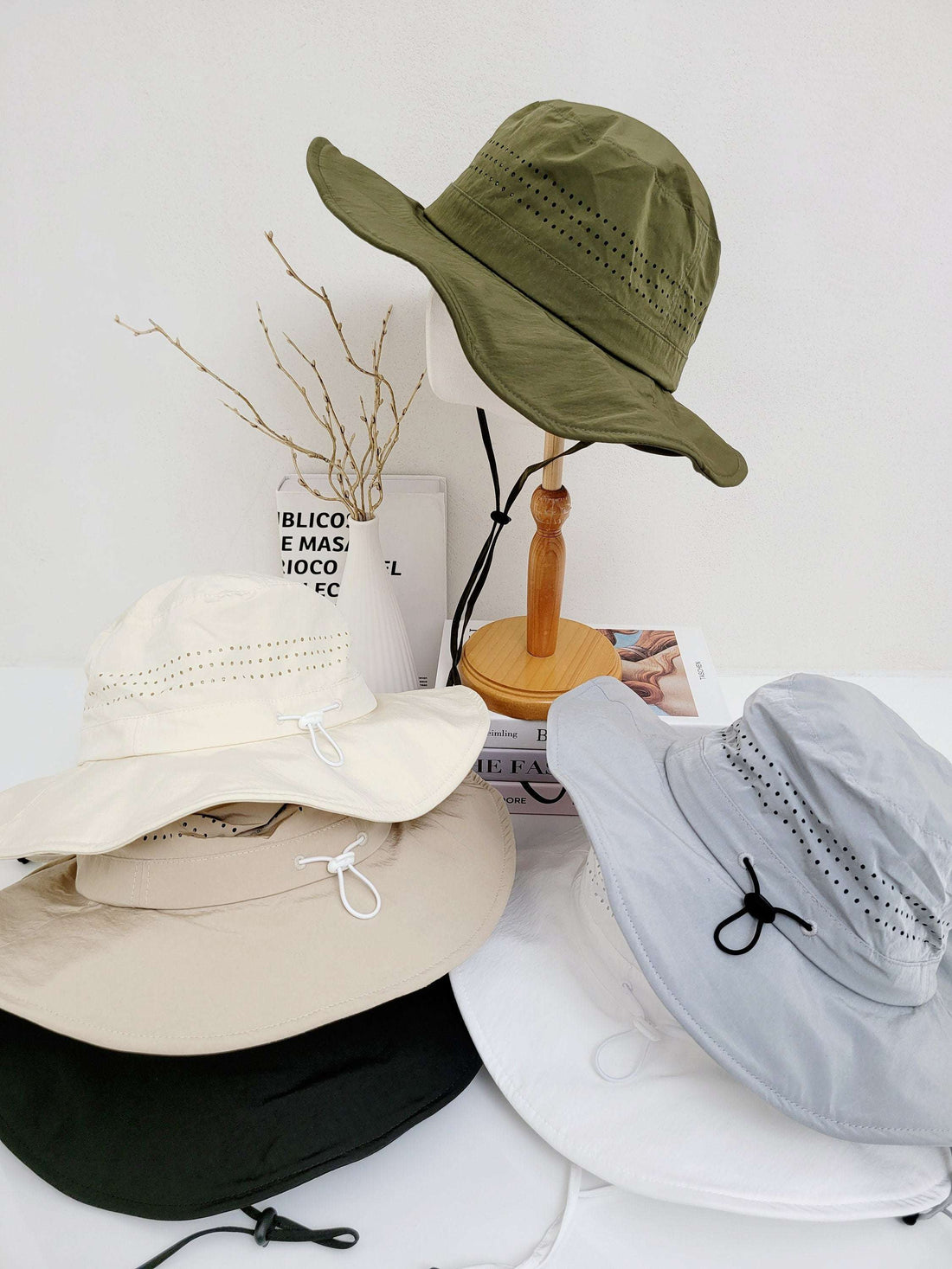 Stack of long journey sun hats in olive, cream, beige, black, light blue, and white. Wide brim, lightweight, and breathable sun protection with adjustable cords.
