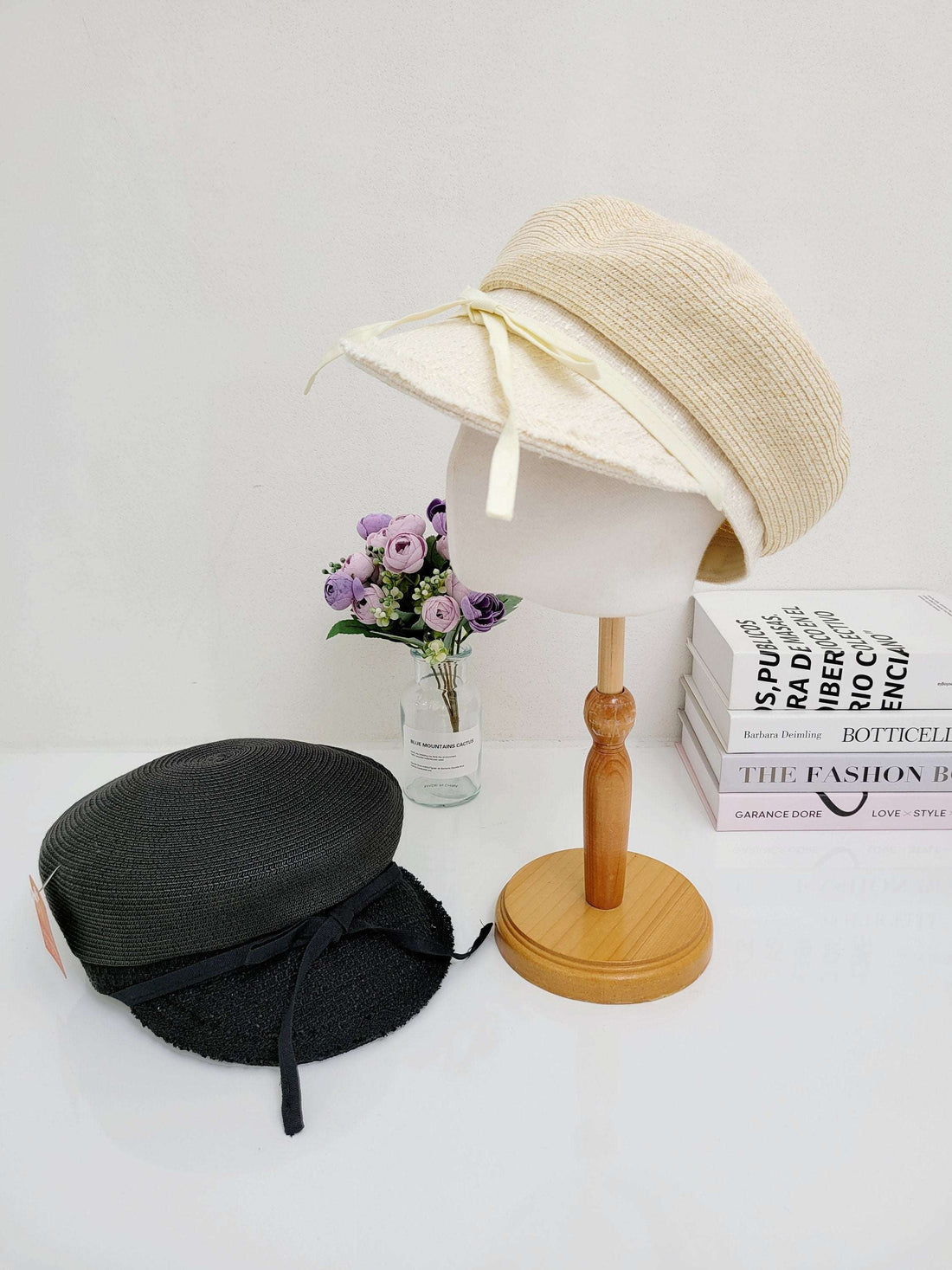 Cream-colored knit hat on a stand next to a black hat with ribbon detail, showcasing the grace collection.