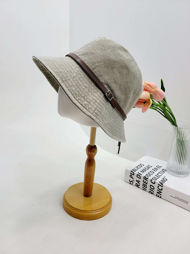 MILES gray bucket hat with a stylish brown leather band detail, displayed on a wooden stand.
