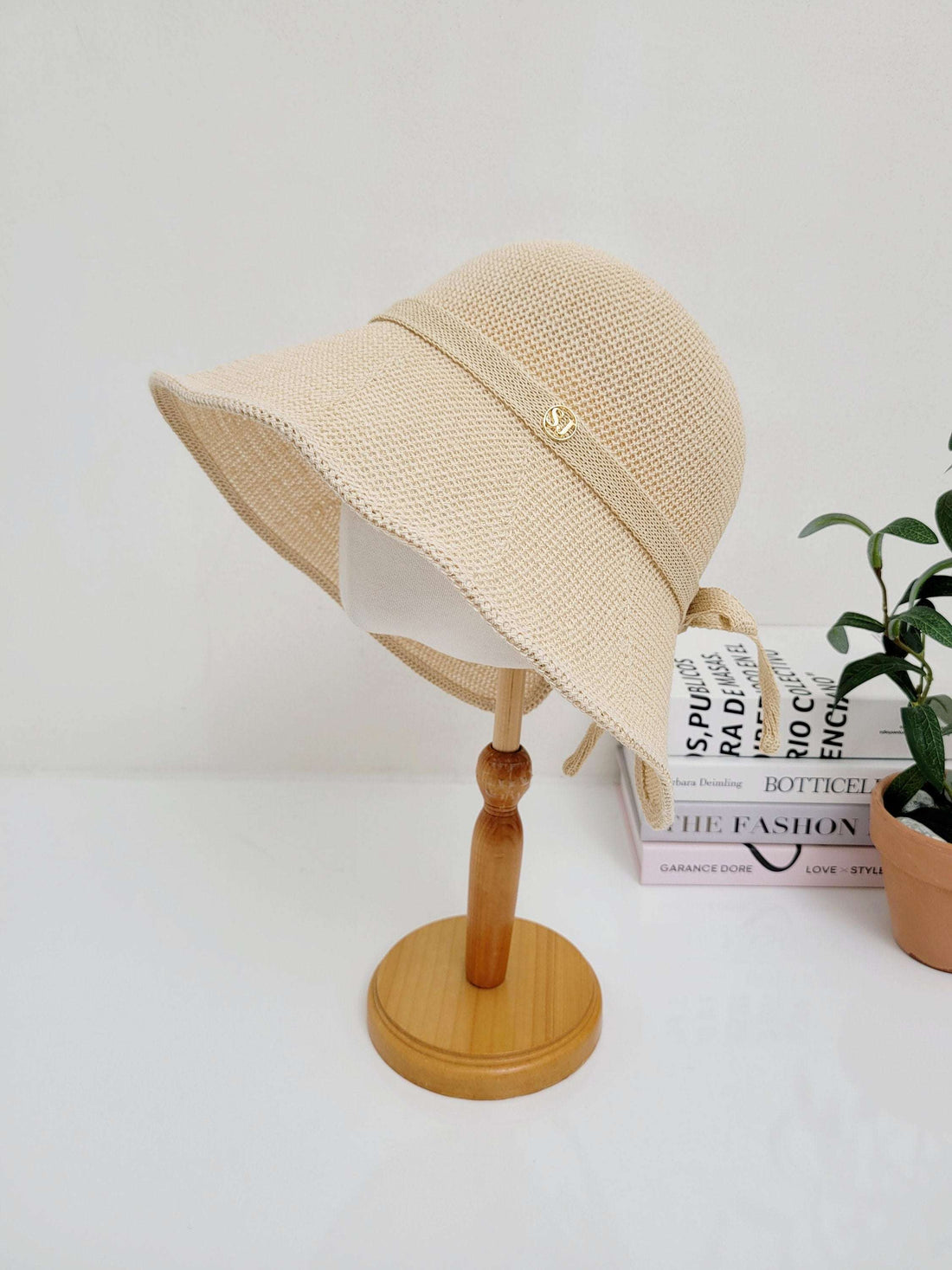 Beige woven sun hat with a stylish brim and ribbon accent, displayed on a wooden stand, perfect for sun protection and summer style.