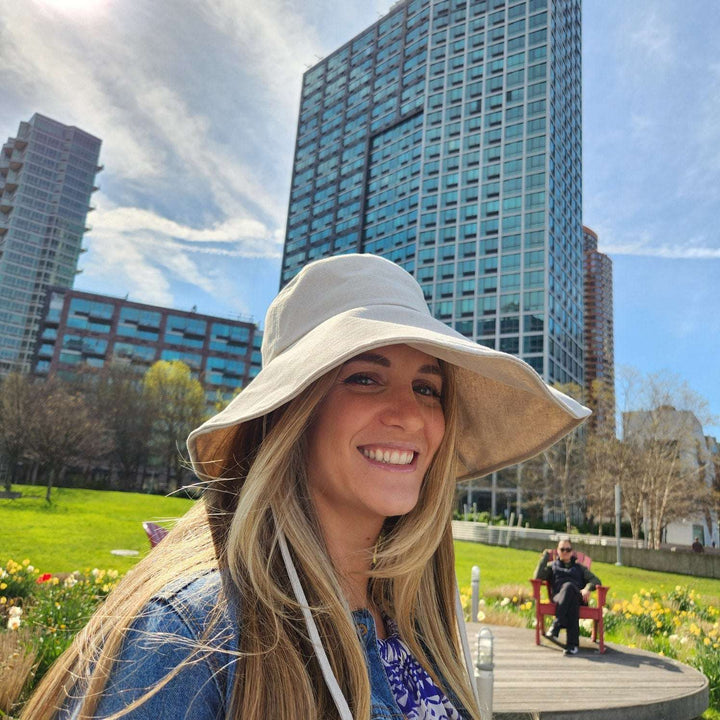 Woman wearing a cotton linen wide brim-solid hat. Neutral-toned sun hat with a wide brim for sun protection, in a park setting.