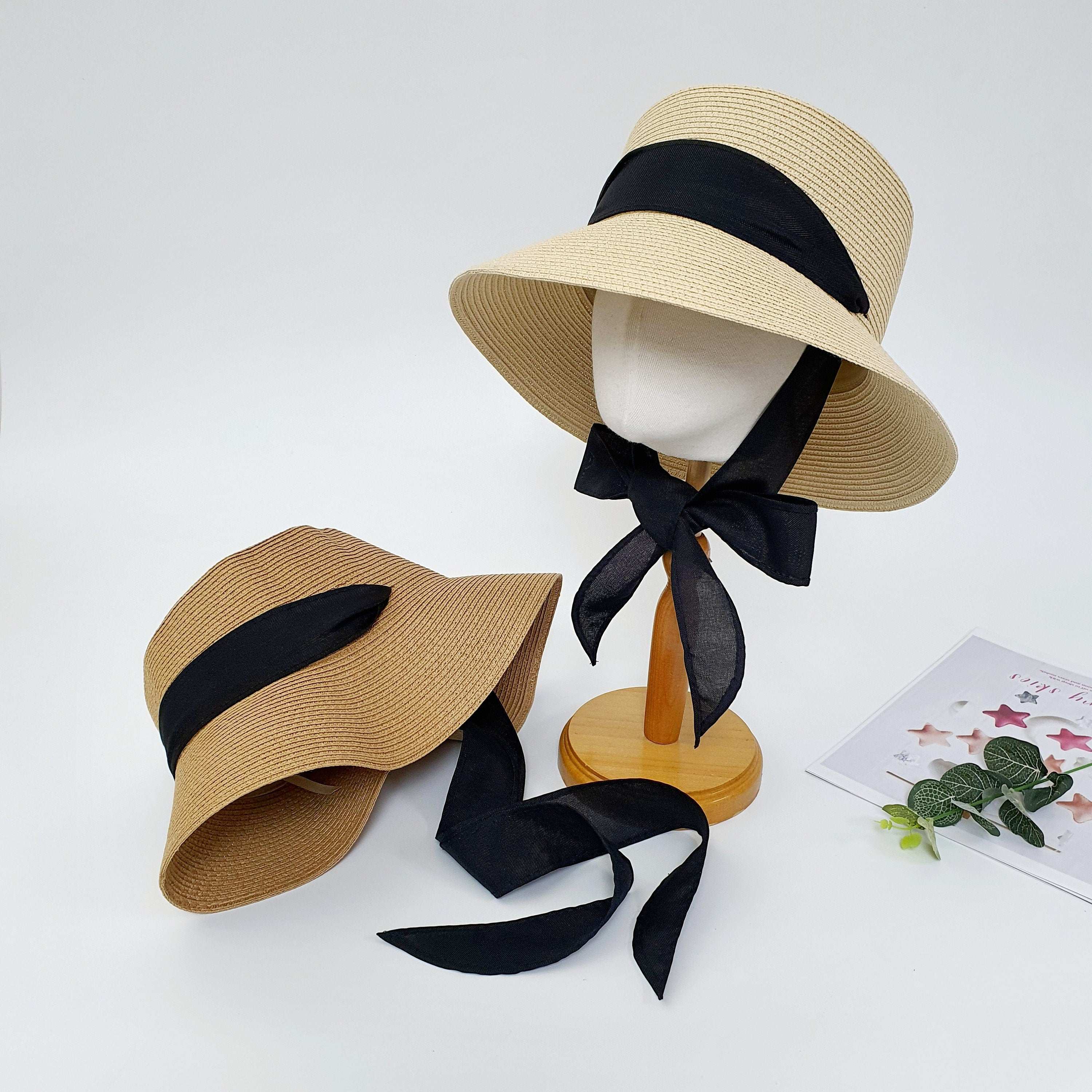 Two straw hats, one tan and one light beige, both with wide brims and a black ribbon tie. The penelope hat is perfect for sun protection and style.