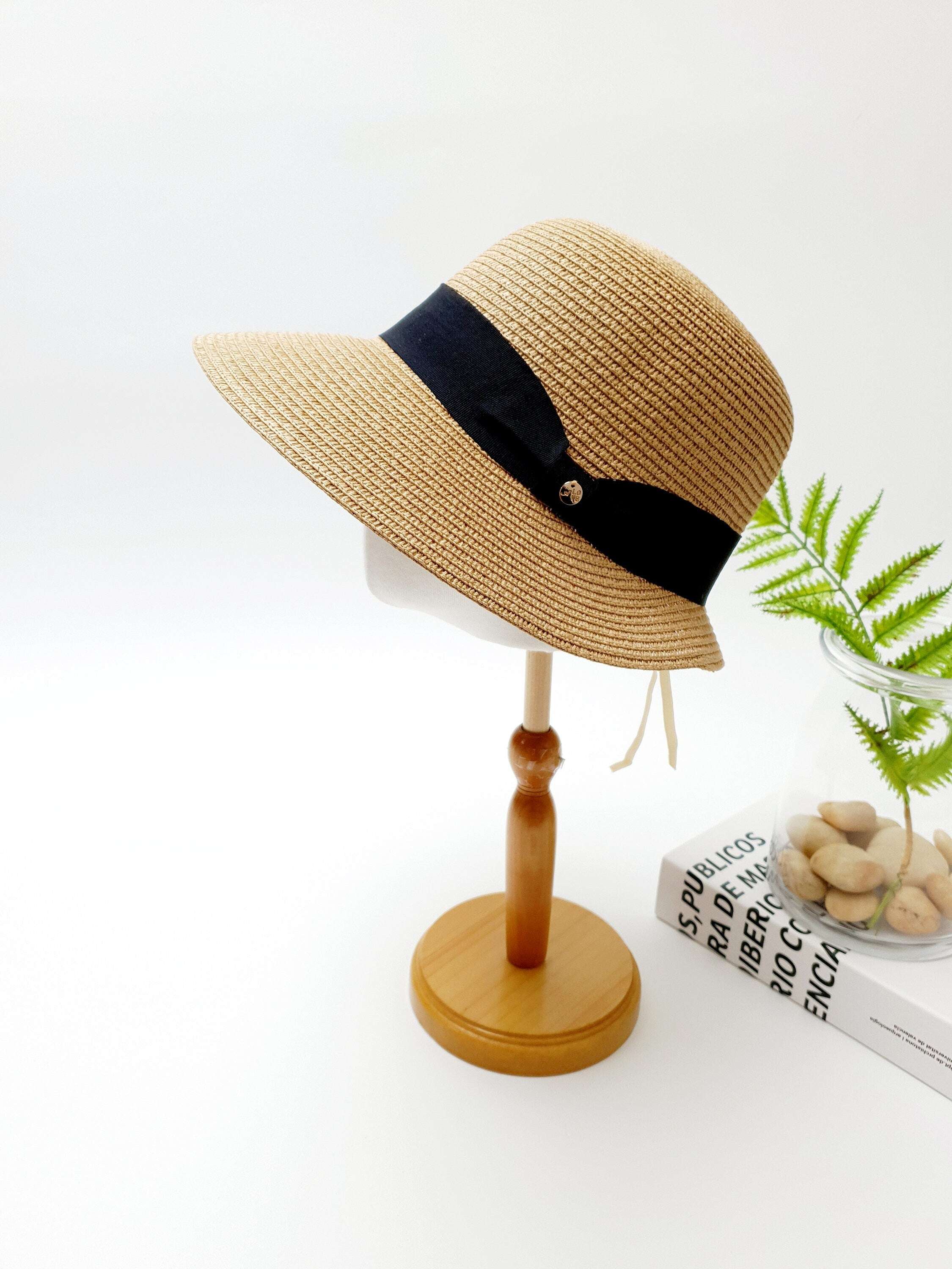 Tan straw isabelle hat with a stylish black ribbon accent, displayed on a wooden stand.