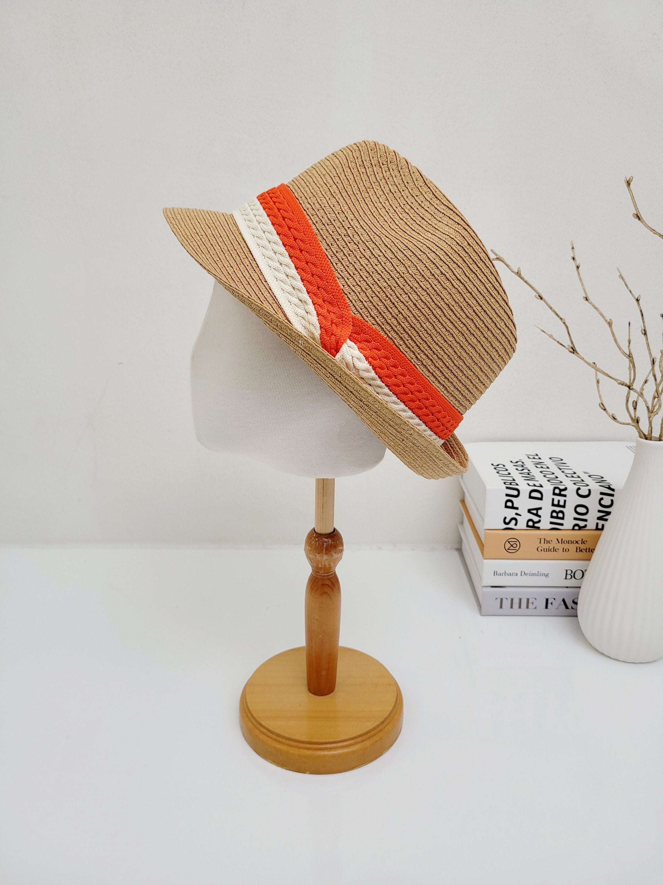 Tan raffia fedora with a striking orange and white two-tone band, displayed on a mannequin head. A stylish summer hat.
