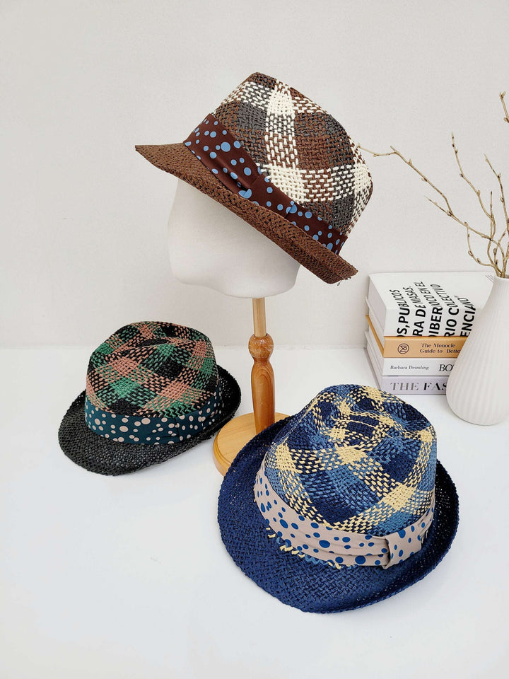 Three breezy fedora hats: brown plaid on a stand, green/black plaid, and blue plaid, all with polka-dot bands on a white table.