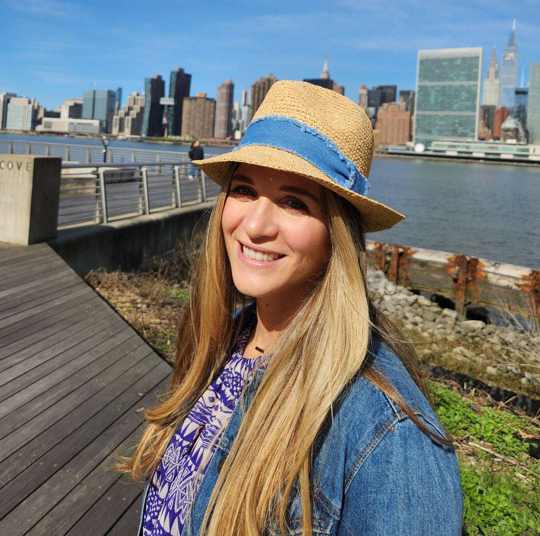Straw sun hat with a blue denim band, worn outdoors with a city skyline in the background