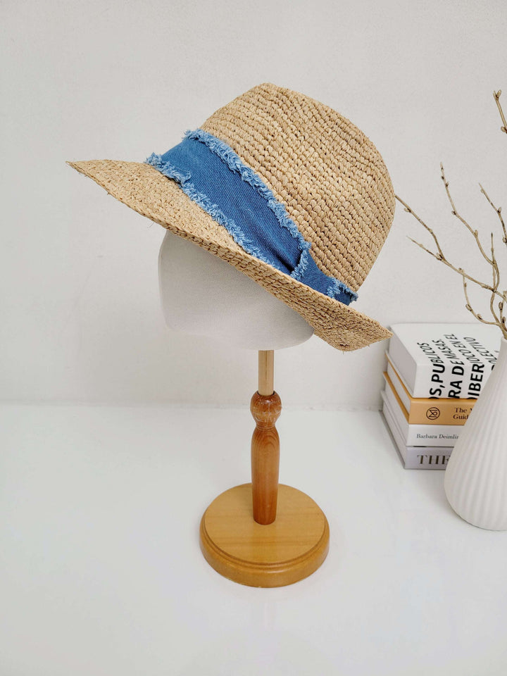 Straw lic breeze hat with a frayed blue denim band, displayed on a wooden stand.