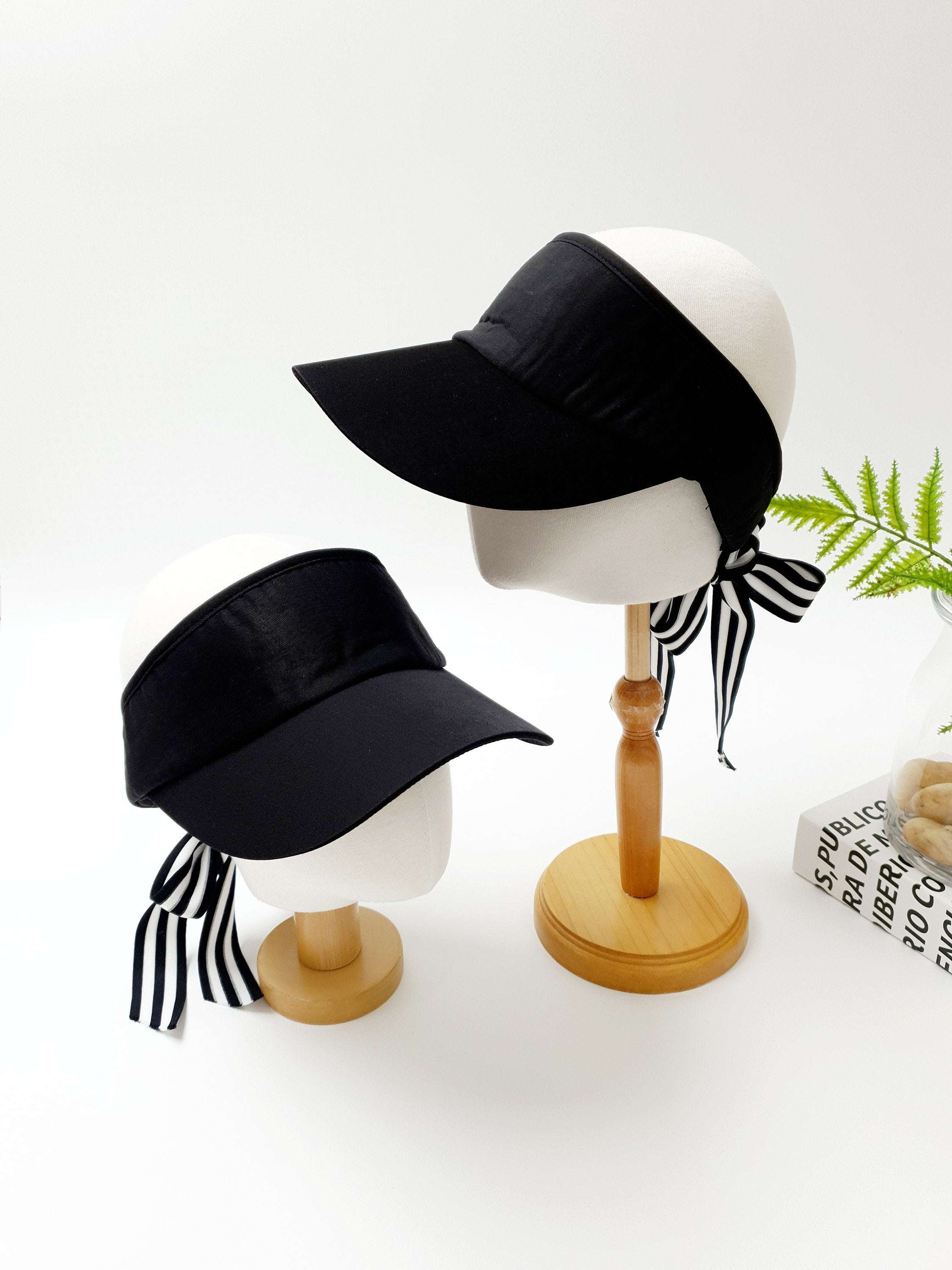 Two mannequin heads display black lic visors with striped ribbon ties; one larger, showcasing the visor's stylish design.