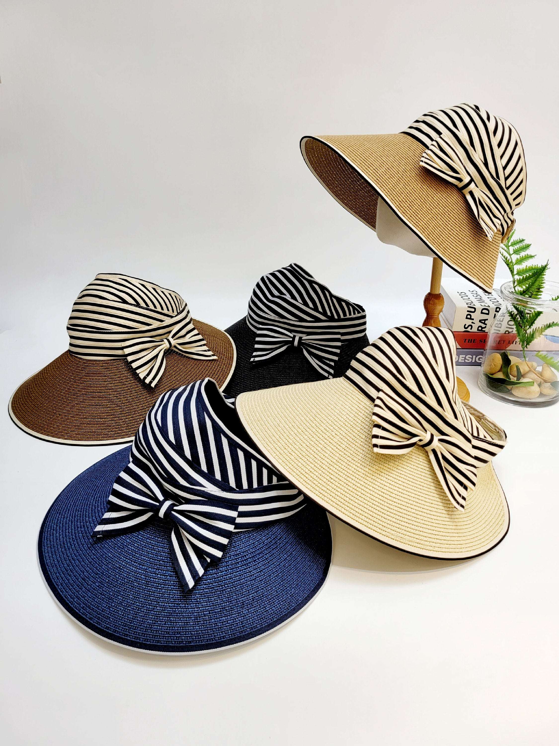 MONROE sun hats: Assorted straw sun hats in brown, black, blue, and beige, each adorned with a stylish black and white striped ribbon bow.