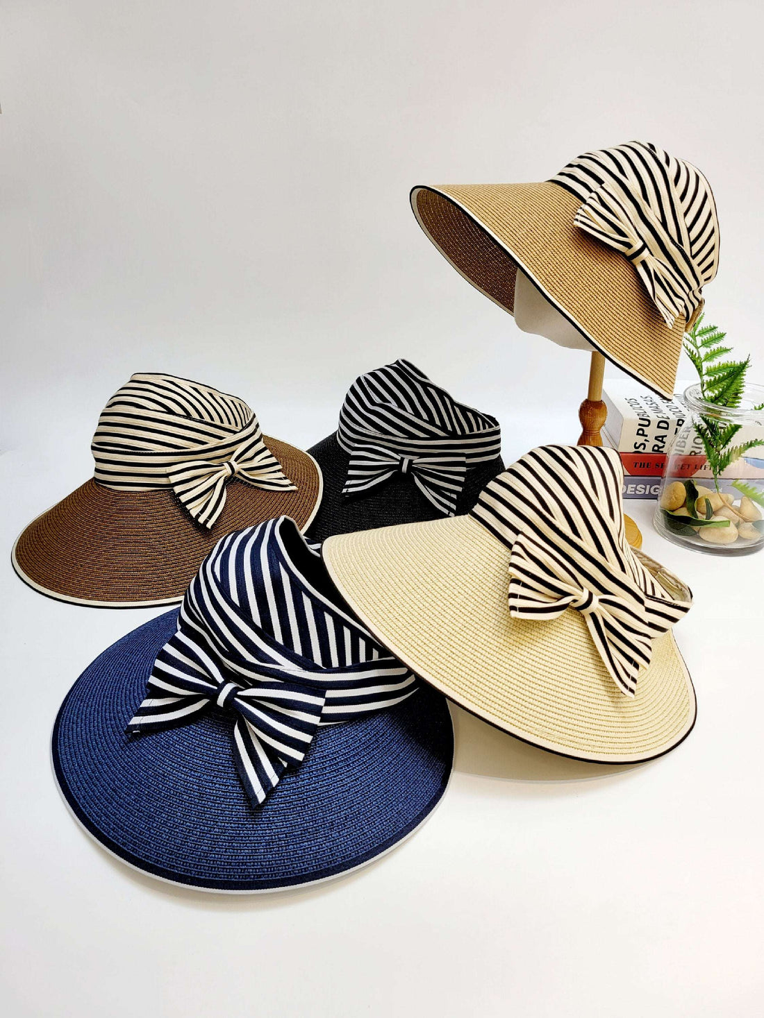 MONROE sun hats: Assorted straw sun hats in brown, black, blue, and beige, each adorned with a stylish black and white striped ribbon bow.