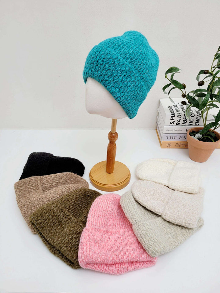 Assorted knit beanies in black, brown, olive, pink, beige, gray, and turquoise, displayed around a mannequin head showcasing the turquoise taylor beanie.