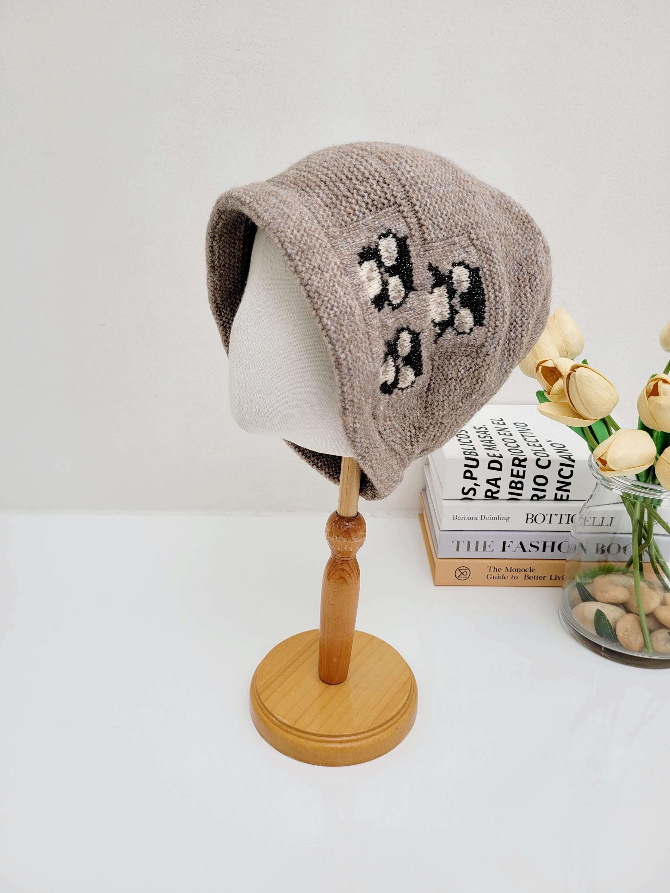 Beige knitted penguin slouch beanie on a mannequin head, featuring embroidered paw print details. A cozy and stylish winter accessory.