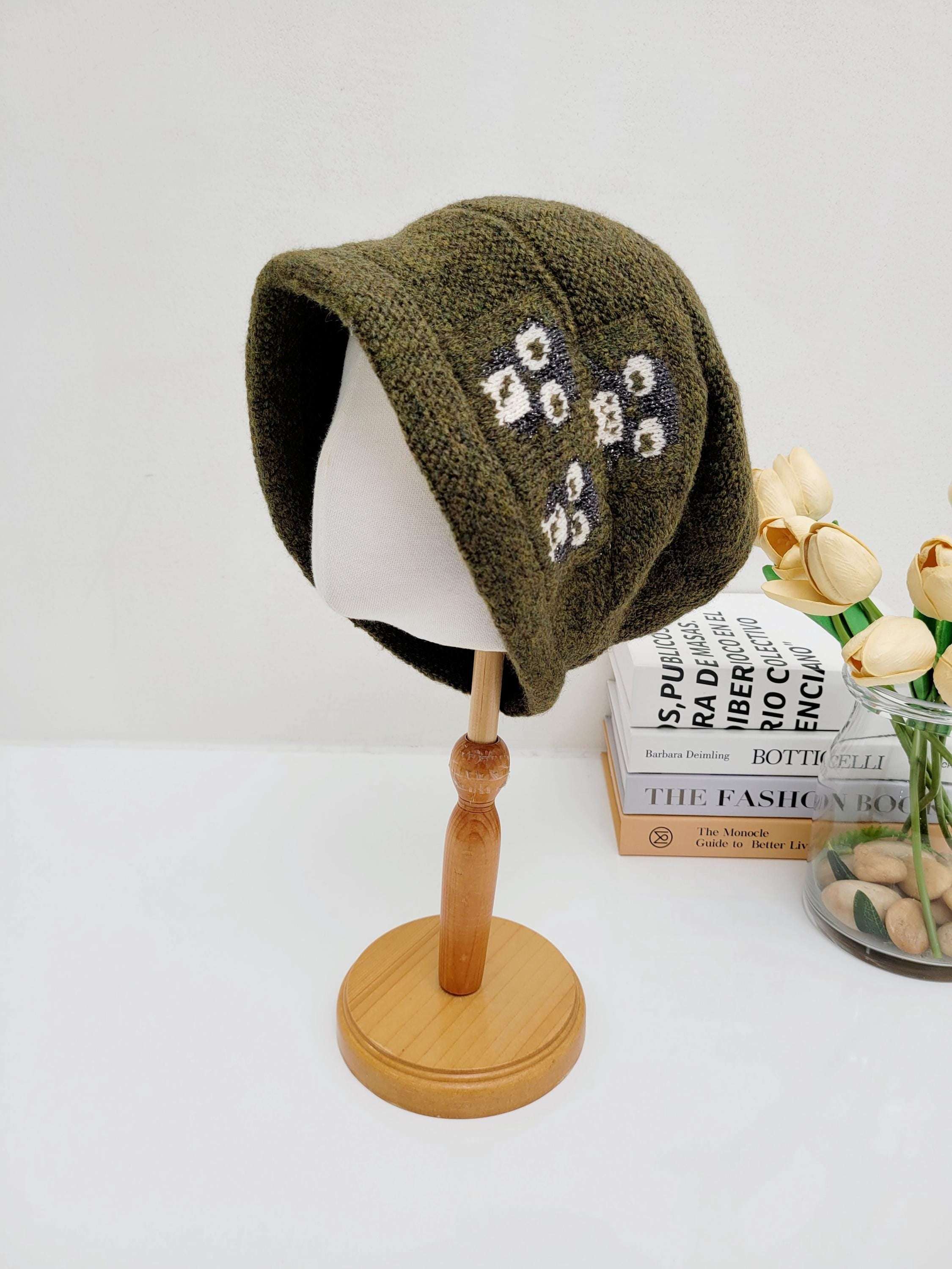Olive green penguin slouch beanie with a subtle white floral pattern, displayed on a wooden stand.