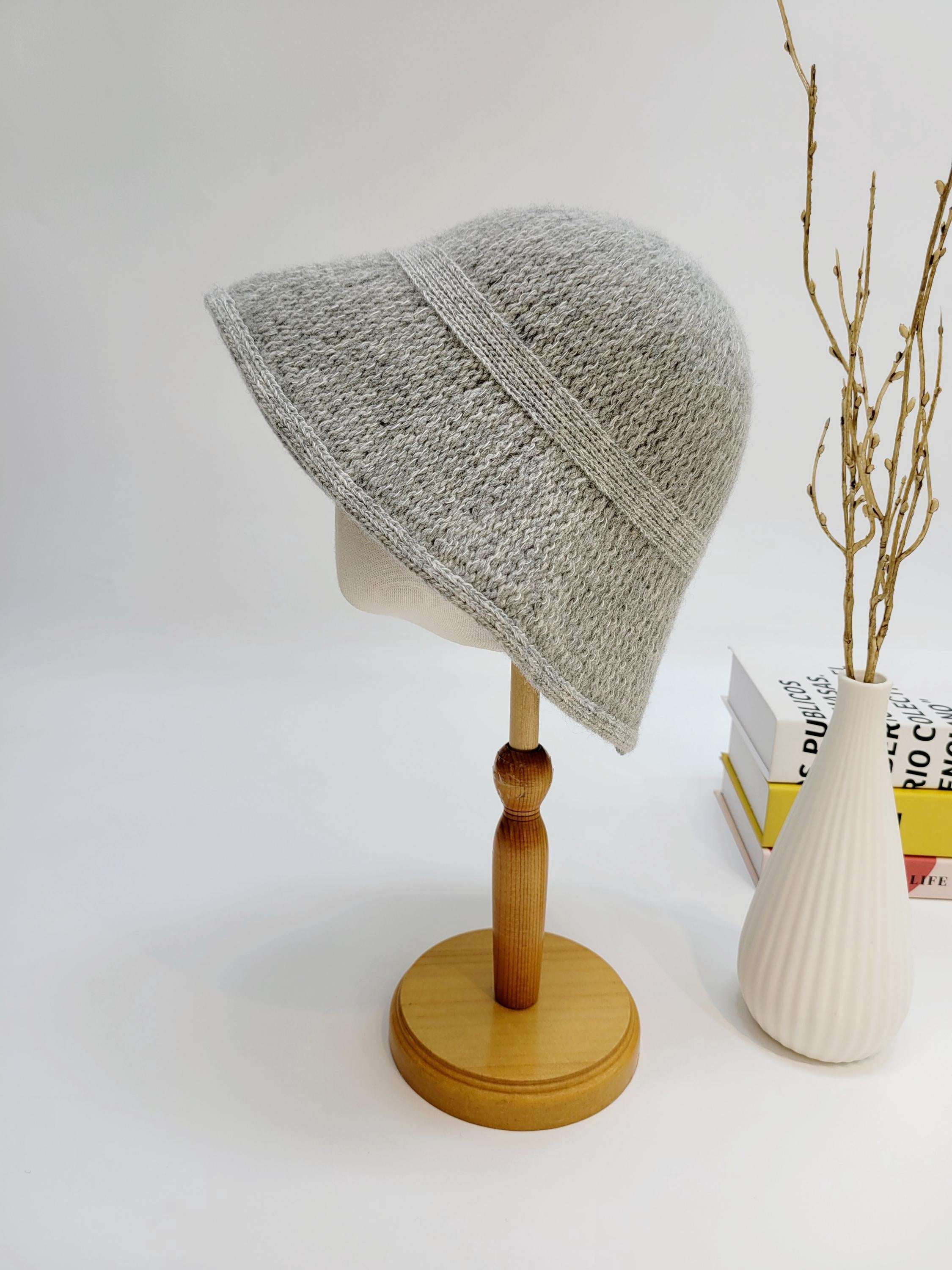 Grey knitted victoria's winter hat on a wooden stand. The hat has a brim and a decorative band.