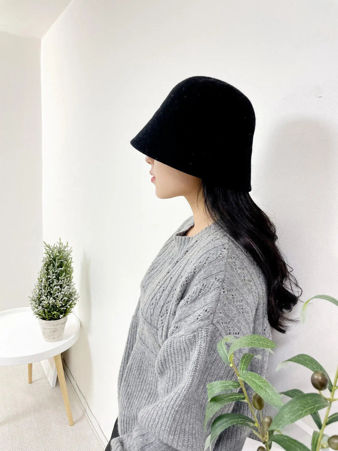 Woman in grey cable-knit sweater wearing a black fall'in winter hat that obscures her eyes.