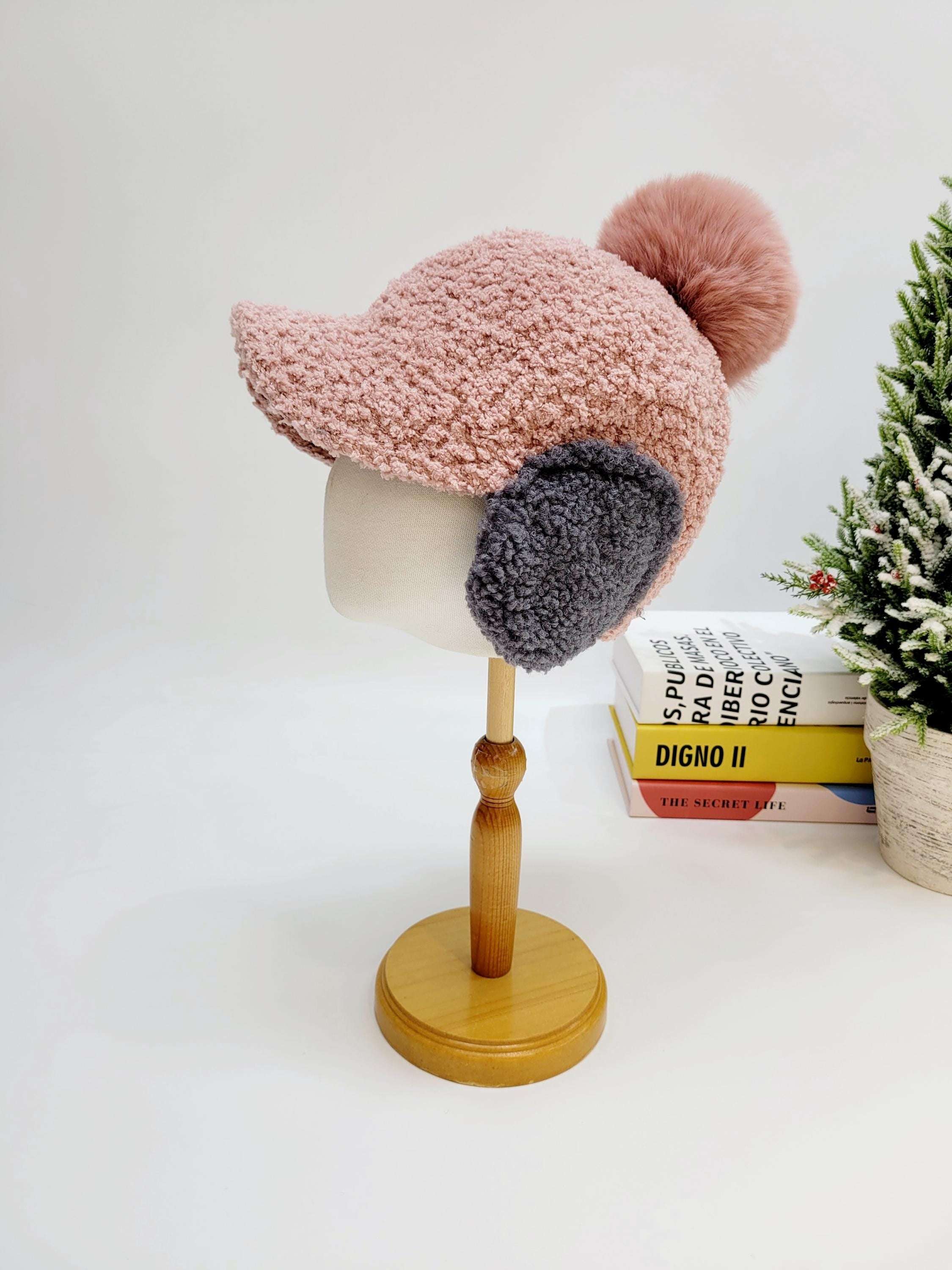 Pink WOOF WOOF textured hat with gray ear flaps and a fluffy pink pompom, displayed on a mannequin head.