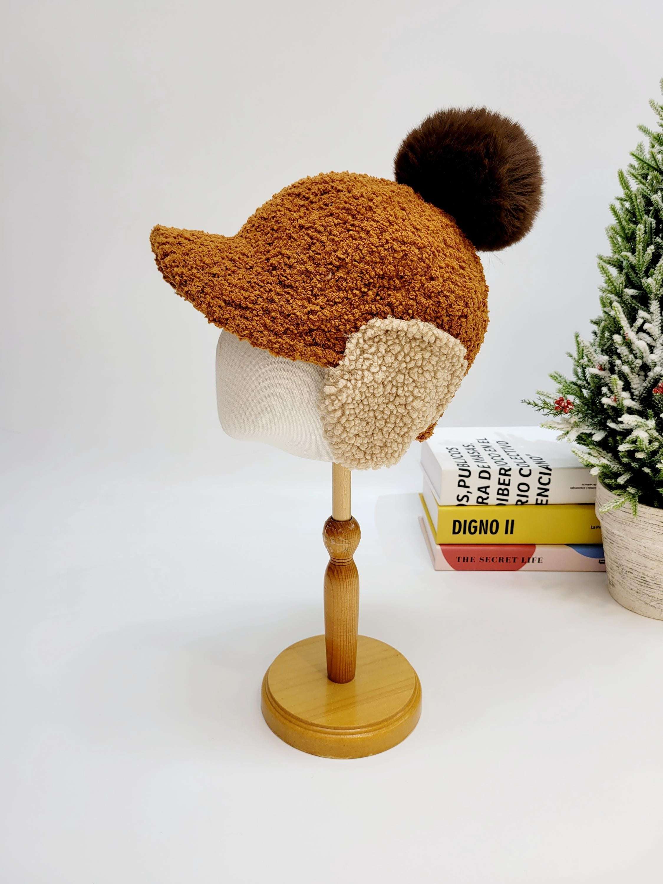 woof woof: Brown textured winter hat with cozy ear flaps and a dark brown pompom, displayed on a mannequin head.