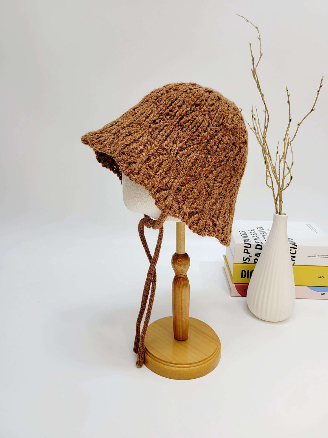 Brown braided wool hat on a wooden stand; hand-knitted with tie strings, a cozy and stylish headwear choice.