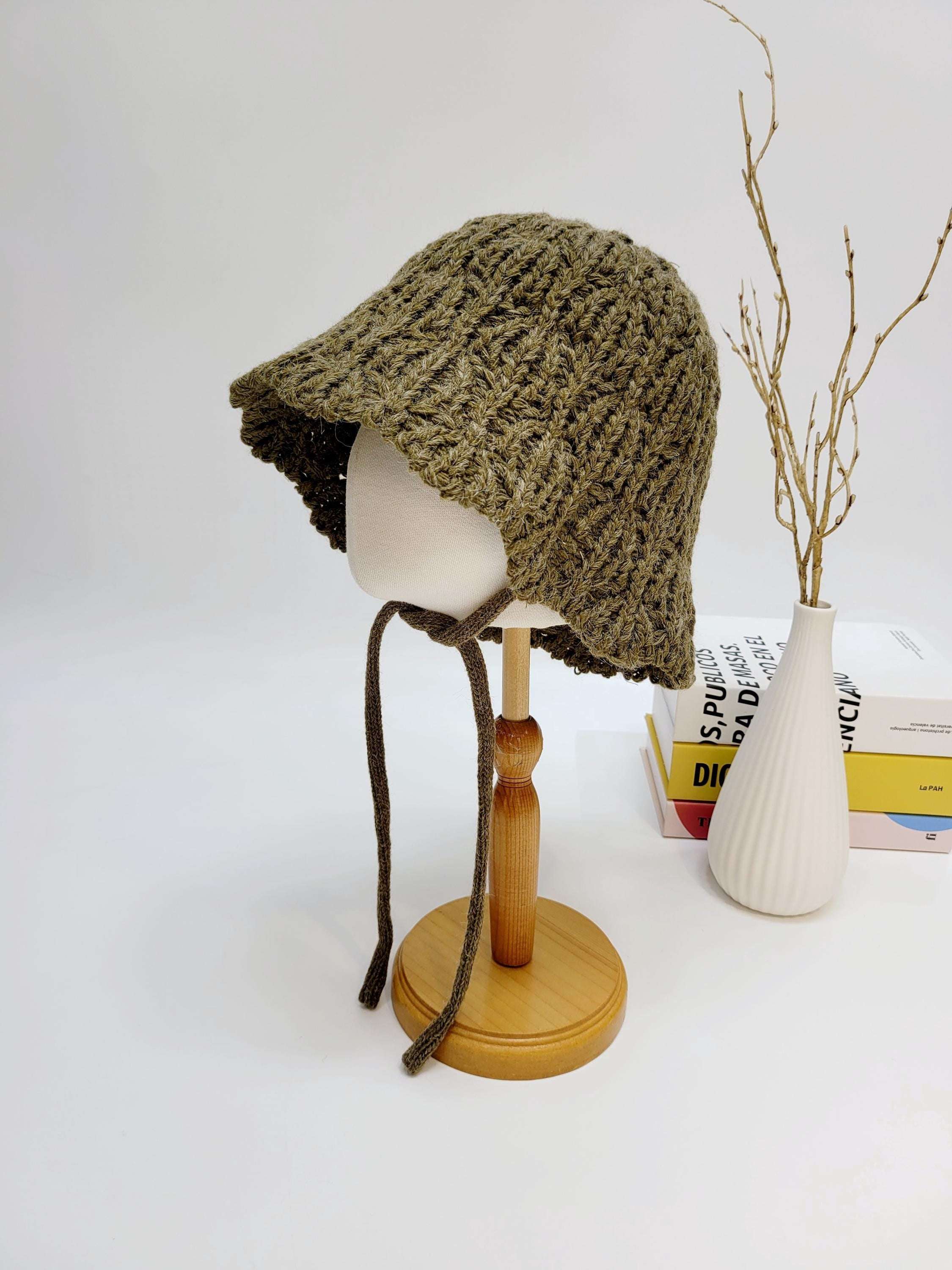 Braided wool hat in olive green, a cozy knitted bucket hat with tie strings displayed on a mannequin head.