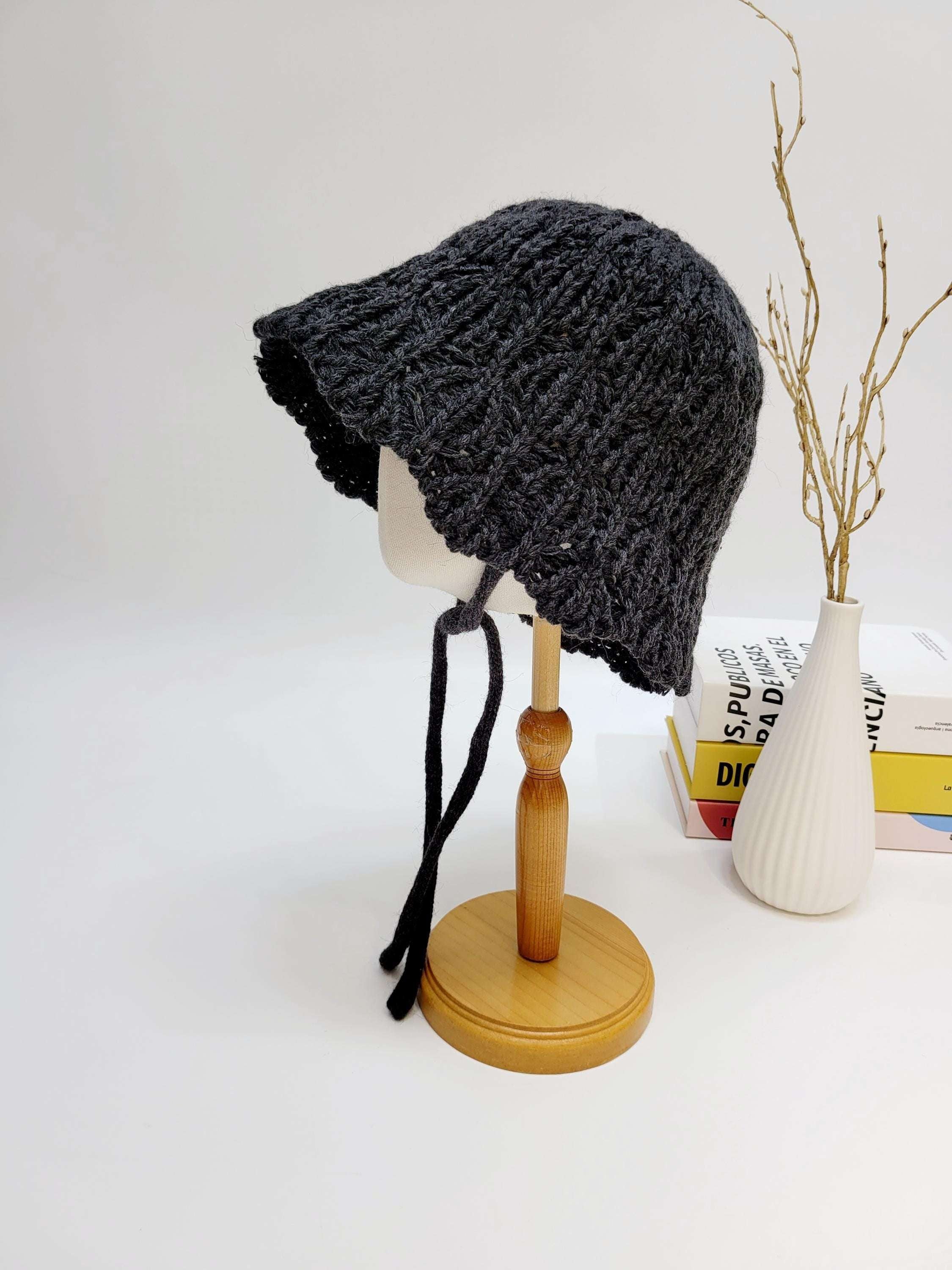 Dark gray braided wool hat with tie strings, displayed on a mannequin head. A cozy and stylish winter accessory.