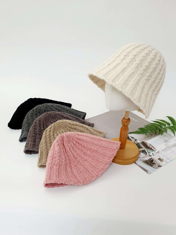 BEANIE THE WOOL-VOL3: Assorted knit bucket hats in black, gray, brown, beige, and pink. A white hat is shown on a mannequin head, highlighting the texture and shape.