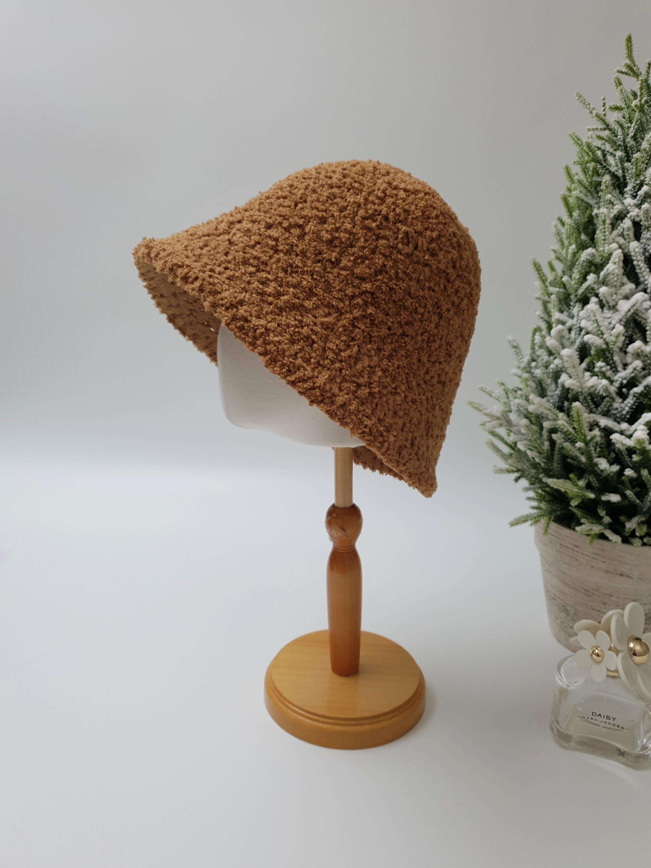 Brown sherpa bucket hat on a wooden display stand. Soft, textured fabric, perfect for a cozy, stylish look.