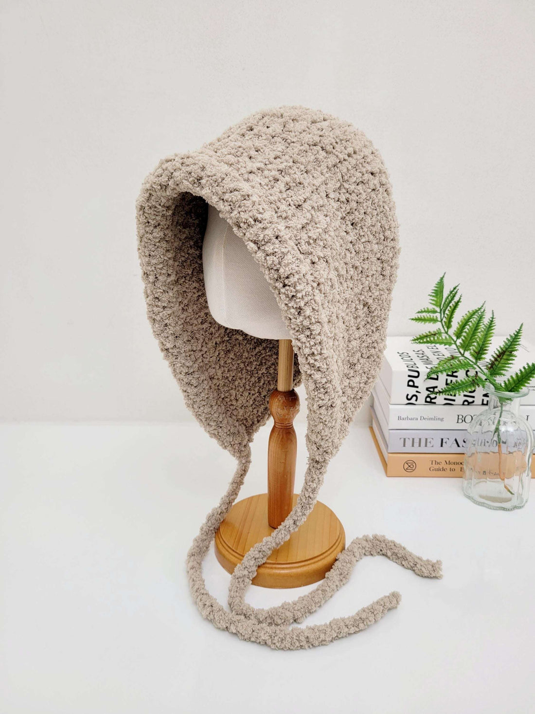 Beige sherpa bonnet, little riding hood - sherpa, with soft texture and tie strings, displayed on a wooden stand.