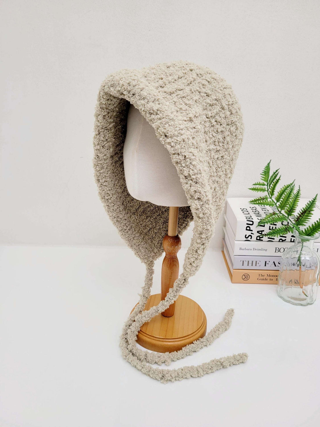 Beige sherpa "little riding hood - sherpa" bonnet on a mannequin head, featuring soft, textured fabric and tie closures.