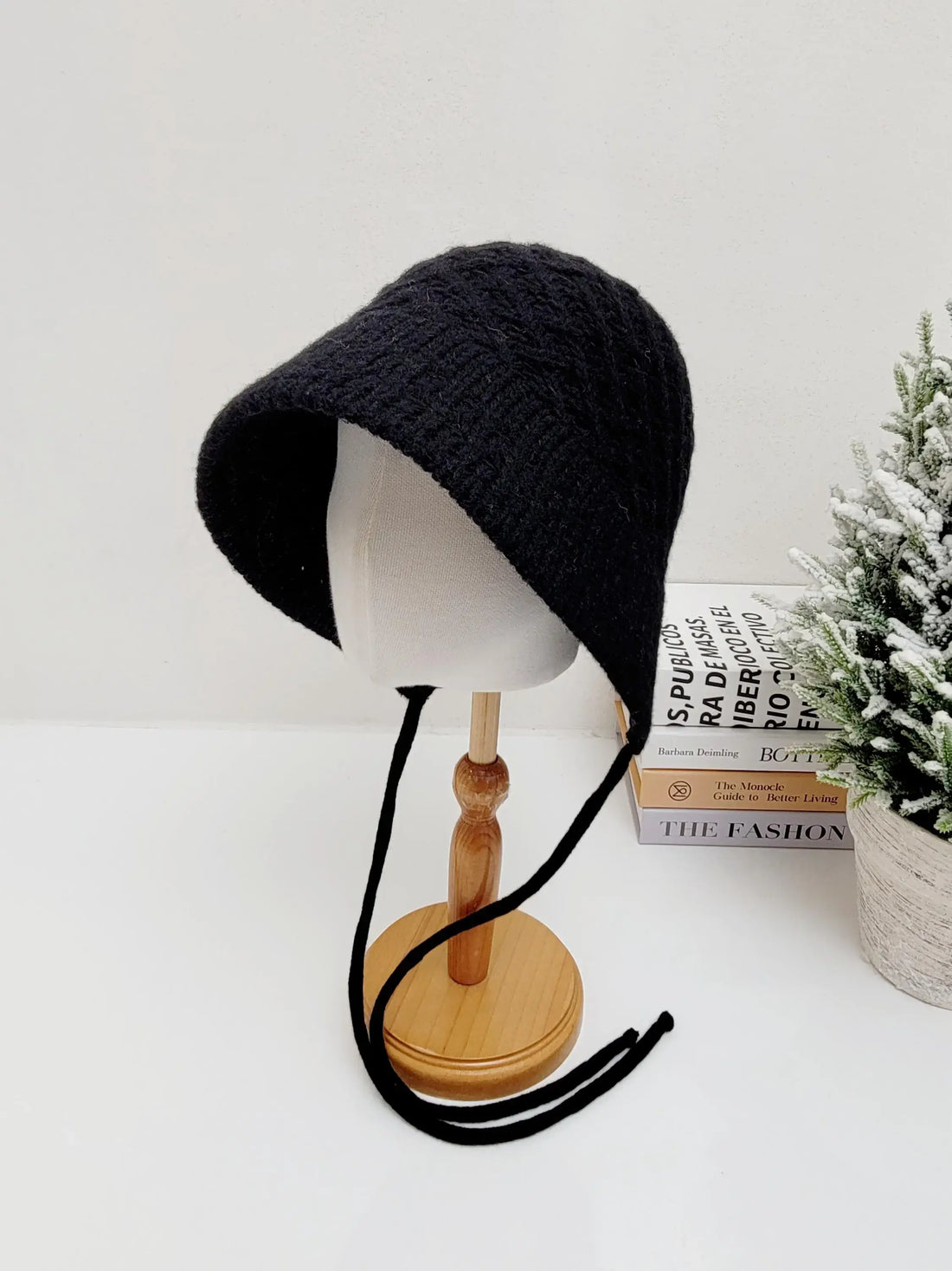 Black knitted wool bucket hat with dangling ties, displayed on a mannequin head. A stylish and cozy headwear choice.