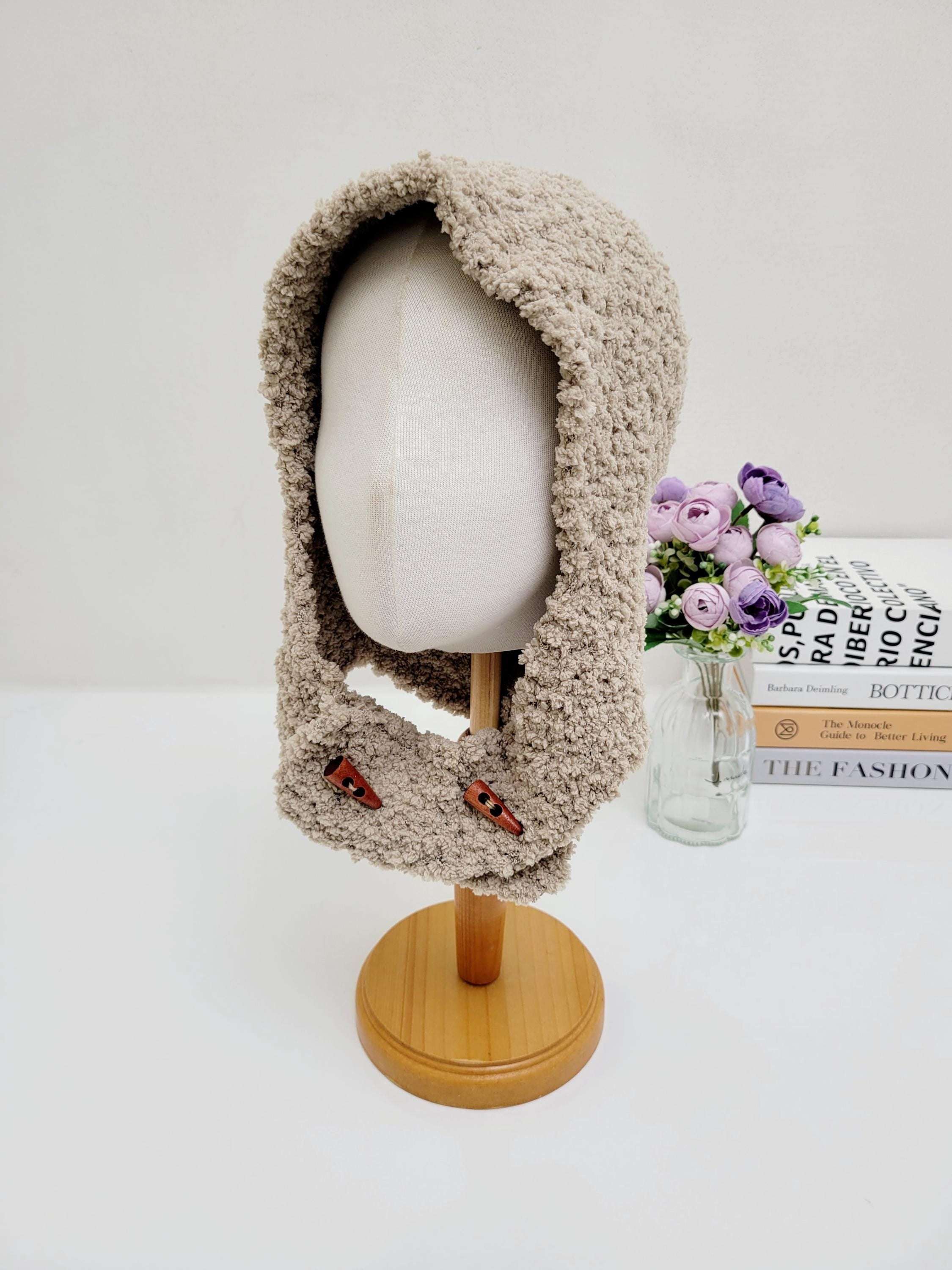 Beige fluffy balaclava on a mannequin head, featuring a soft, textured knit and decorative wooden button details