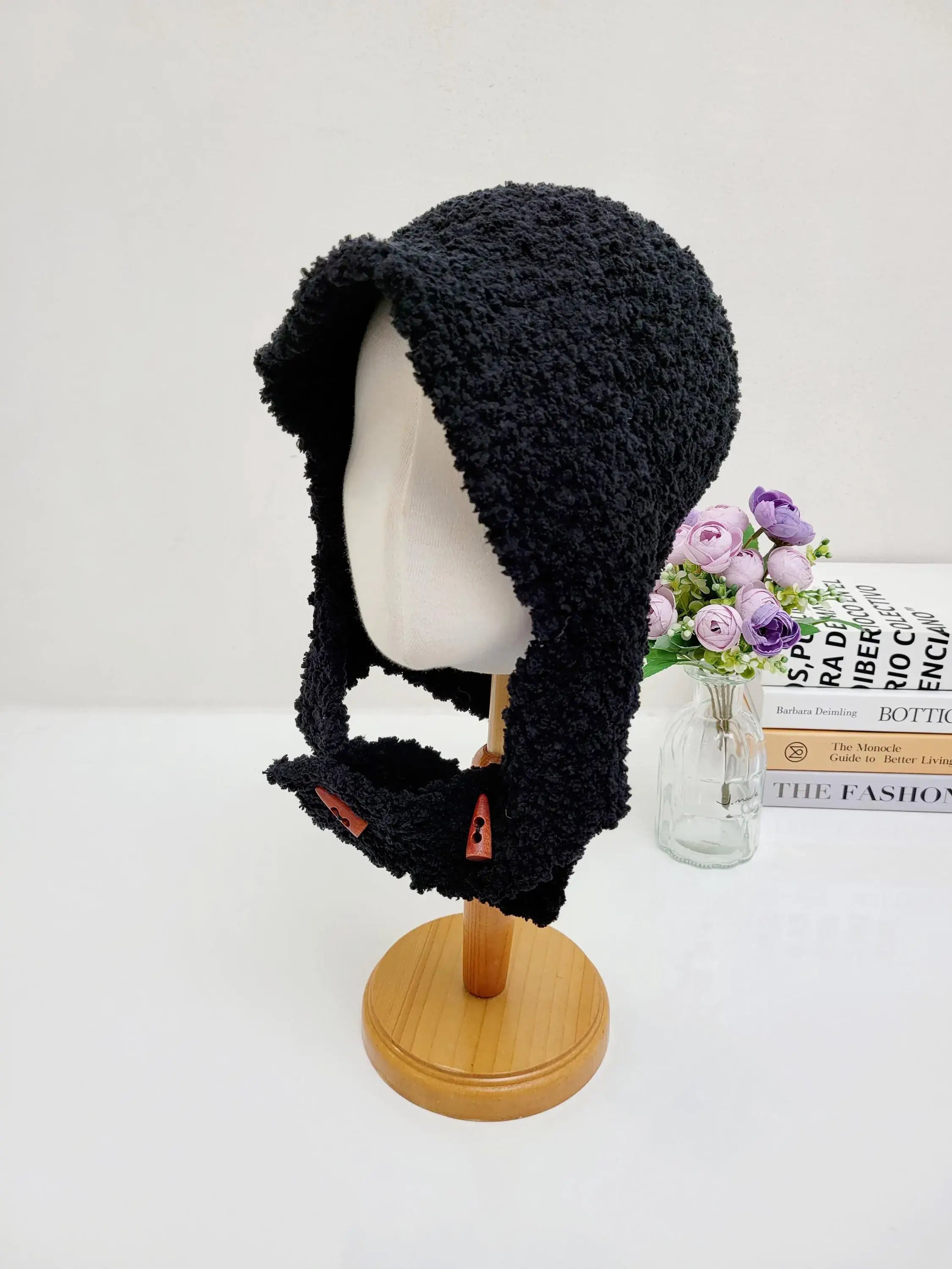 Black fluffy balaclava on a wooden stand, featuring a cozy texture and button details
