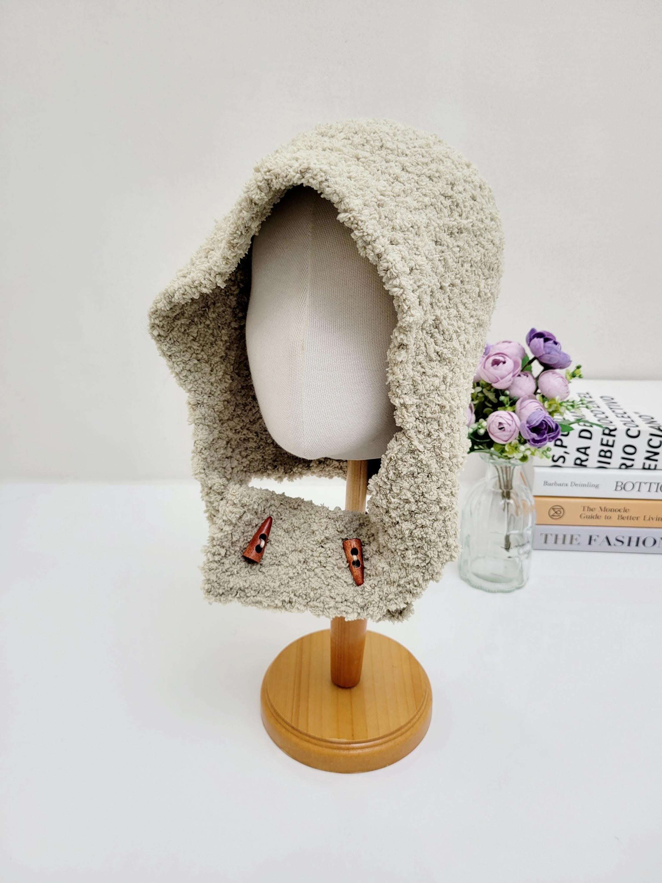 Beige fluffy balaclava on a mannequin, featuring a soft, textured material and button details. The fluffy balaclava offers warmth and style.