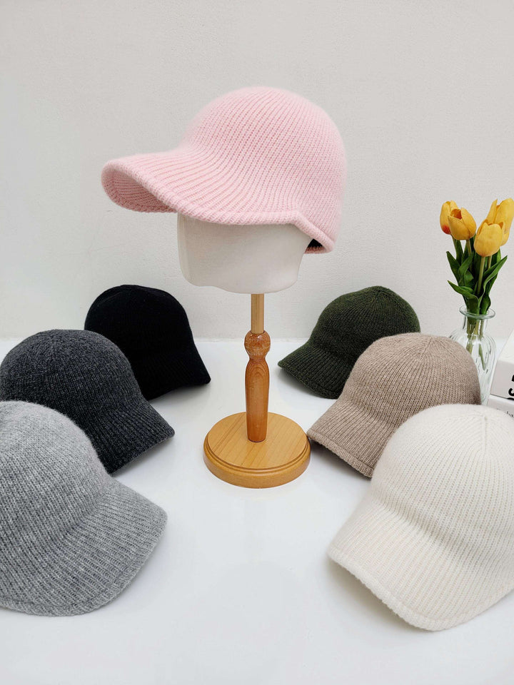Assorted ribbed cap hats. A light pink ribbed cap is on a mannequin head, surrounded by grey, black, olive, beige, and white ribbed caps.