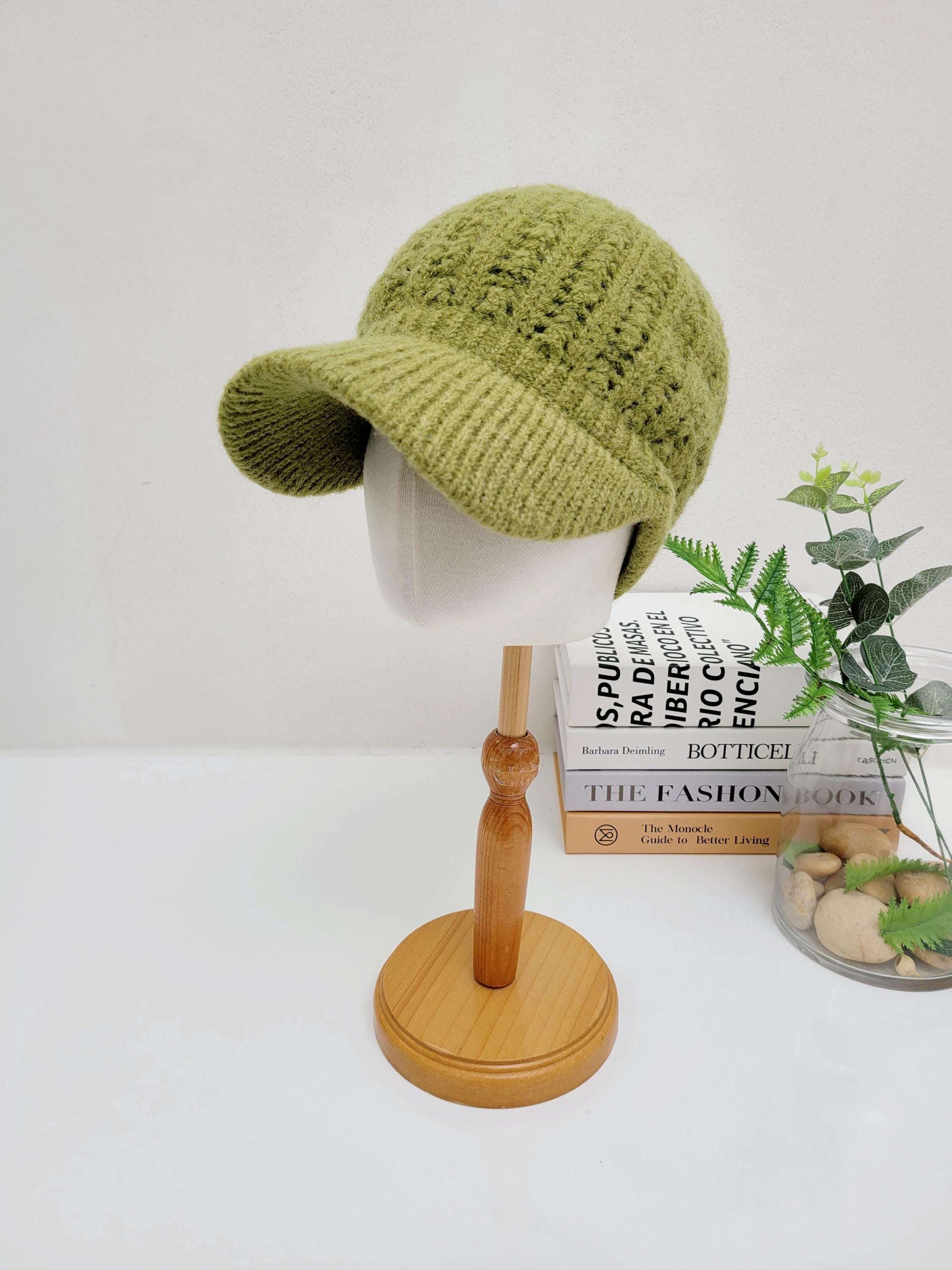 Green crochet baseball cap on a wooden stand. The hat has a short brim and a textured knit design.