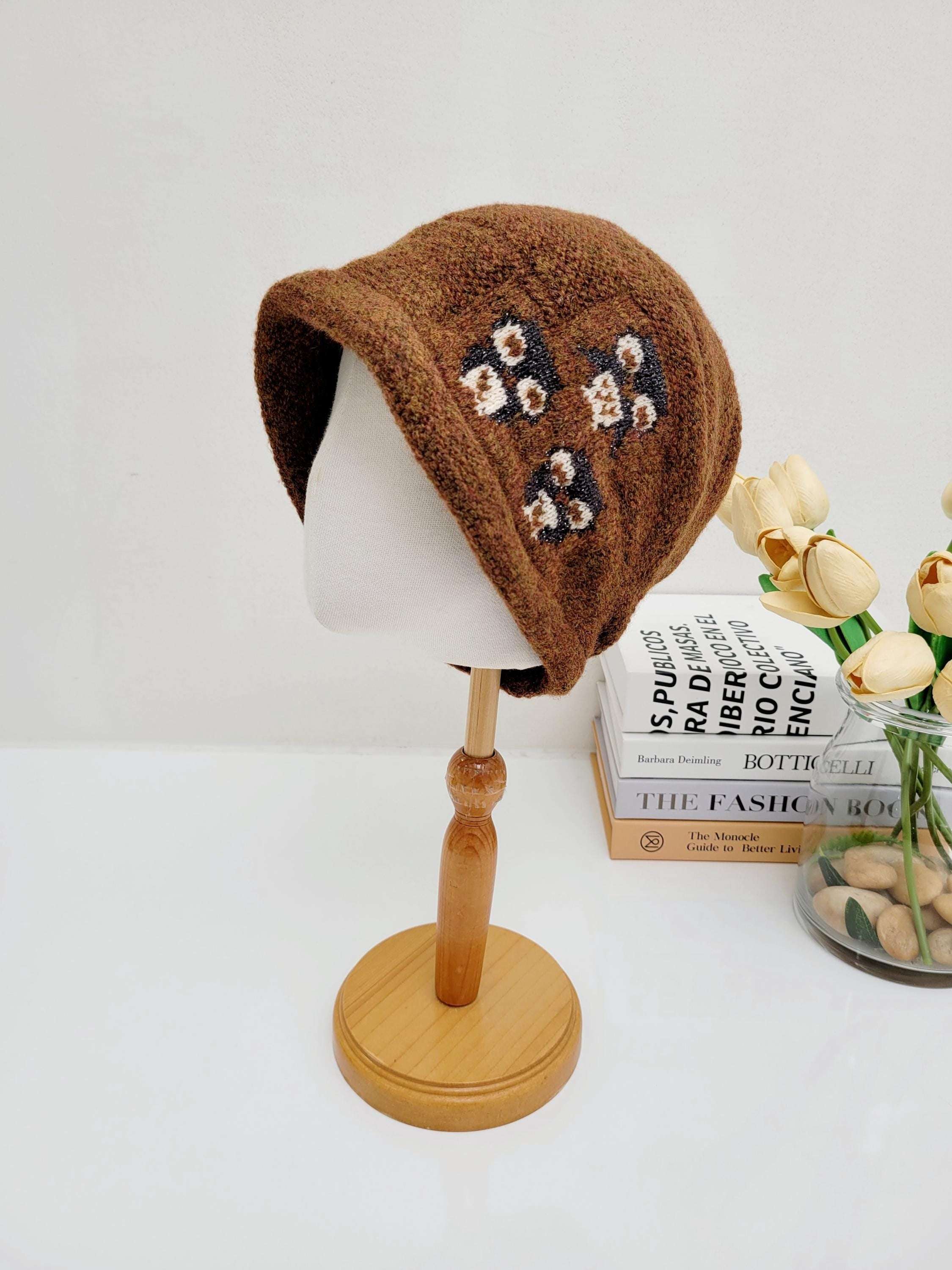 Brown knit penguin slouch beanie with floral details on a mannequin head. Stylish and warm headwear.