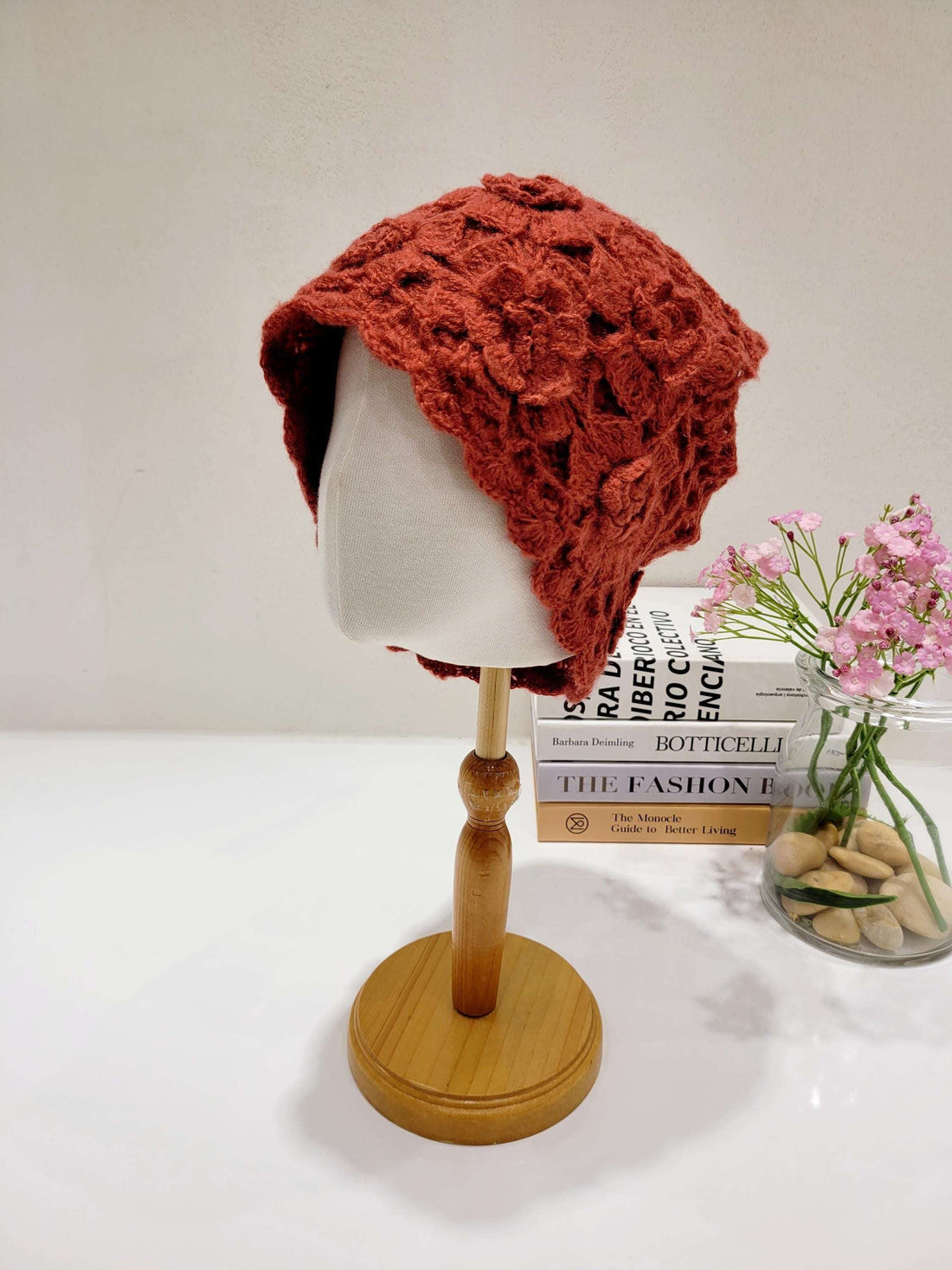 Rust-colored sharon beanie, a textured crochet hat displayed on a wooden stand with books and flowers.